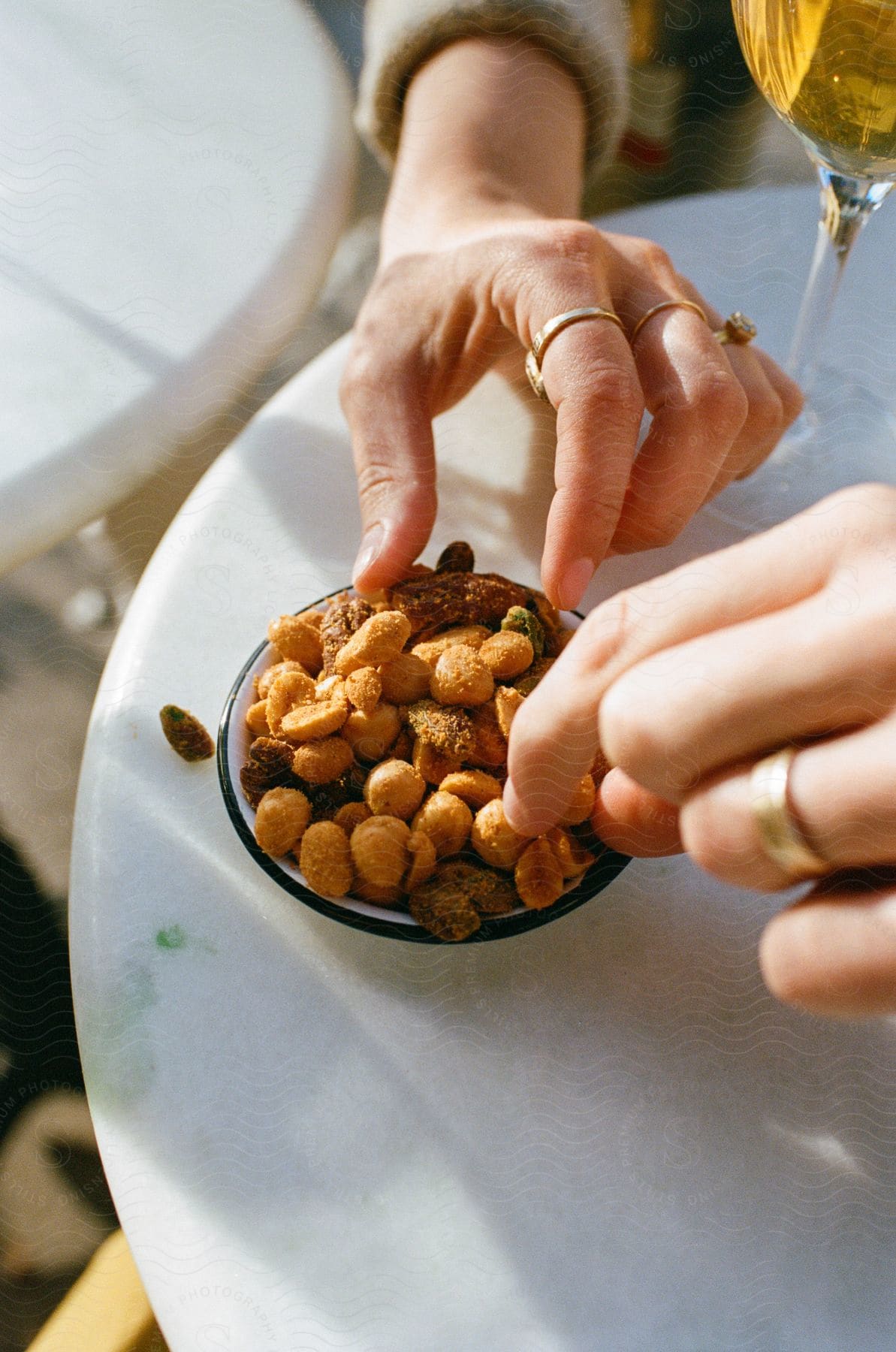 Two peoples hands reach for nuts in a small bowl with a drink on the table