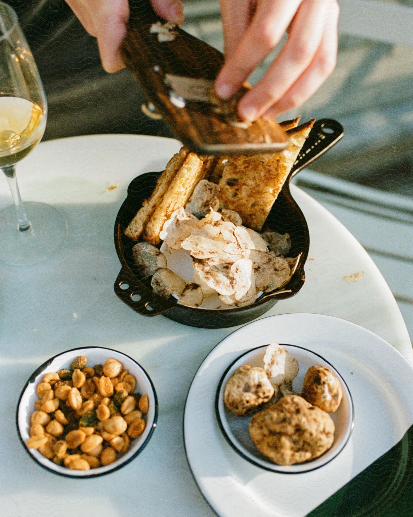 A person is grating spices over a bowl of appetizers at a small dining table.