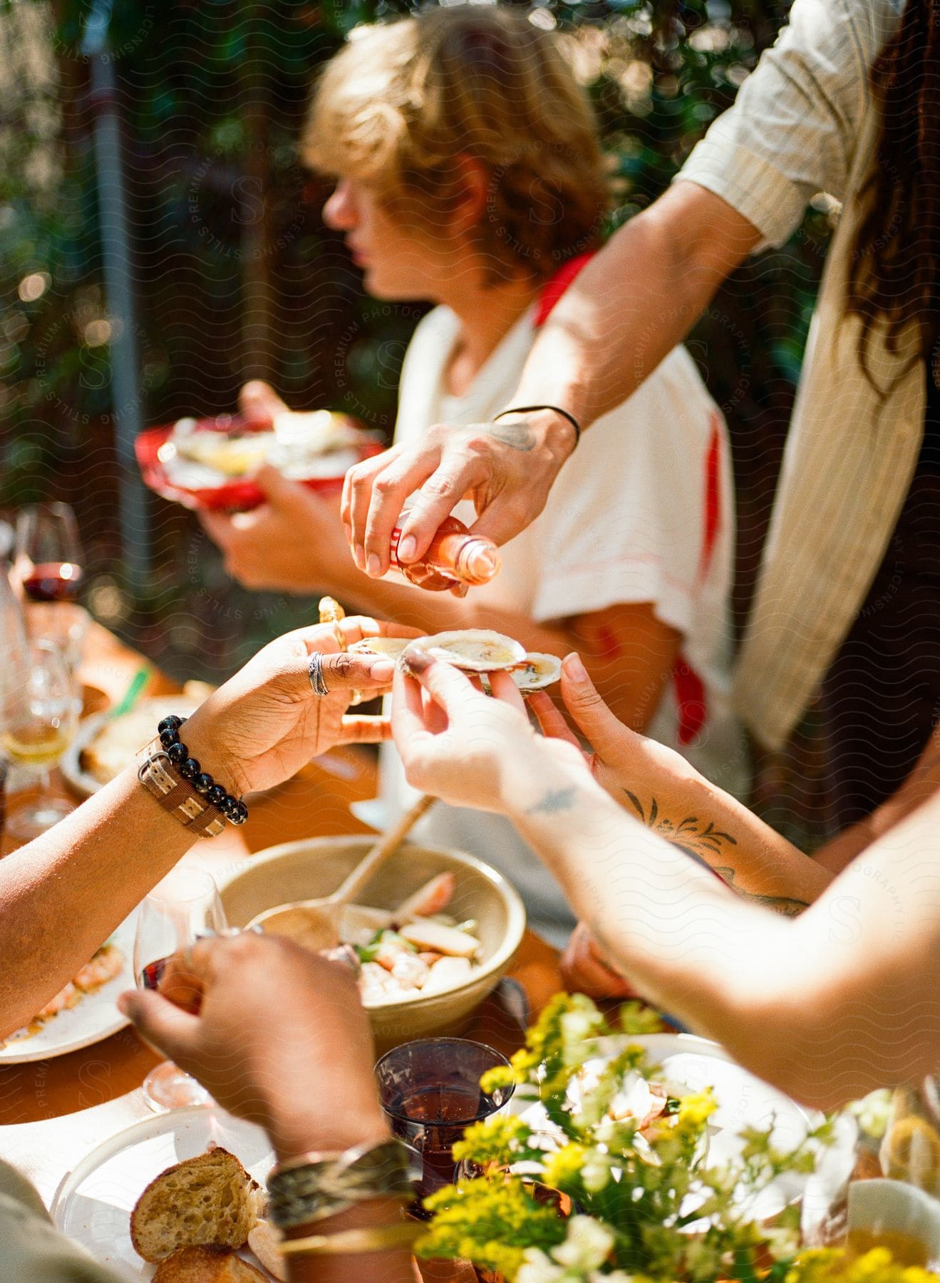 Small group of people sitting around a table of food as a man pours tabasco sauce on oysters as they hold them up over the table