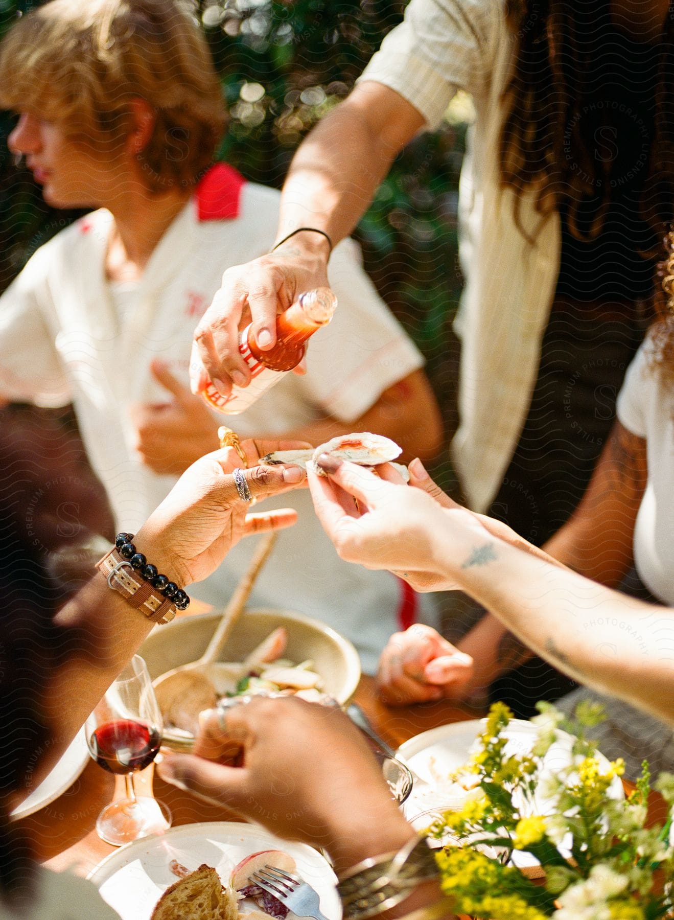 Guests hold up oyster and clam shells for a shot of hot sauce from the host at an outdoor gathering