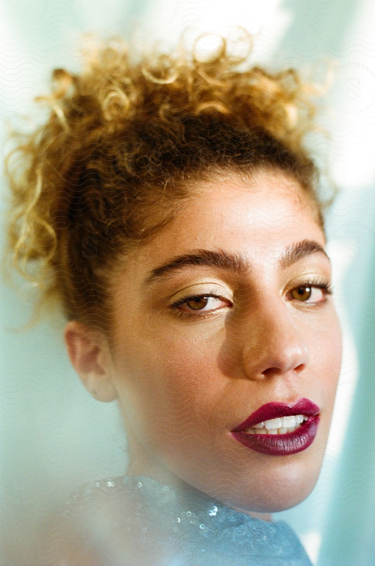 A woman wearing red lipstick and her hair up looks to her side into the camera