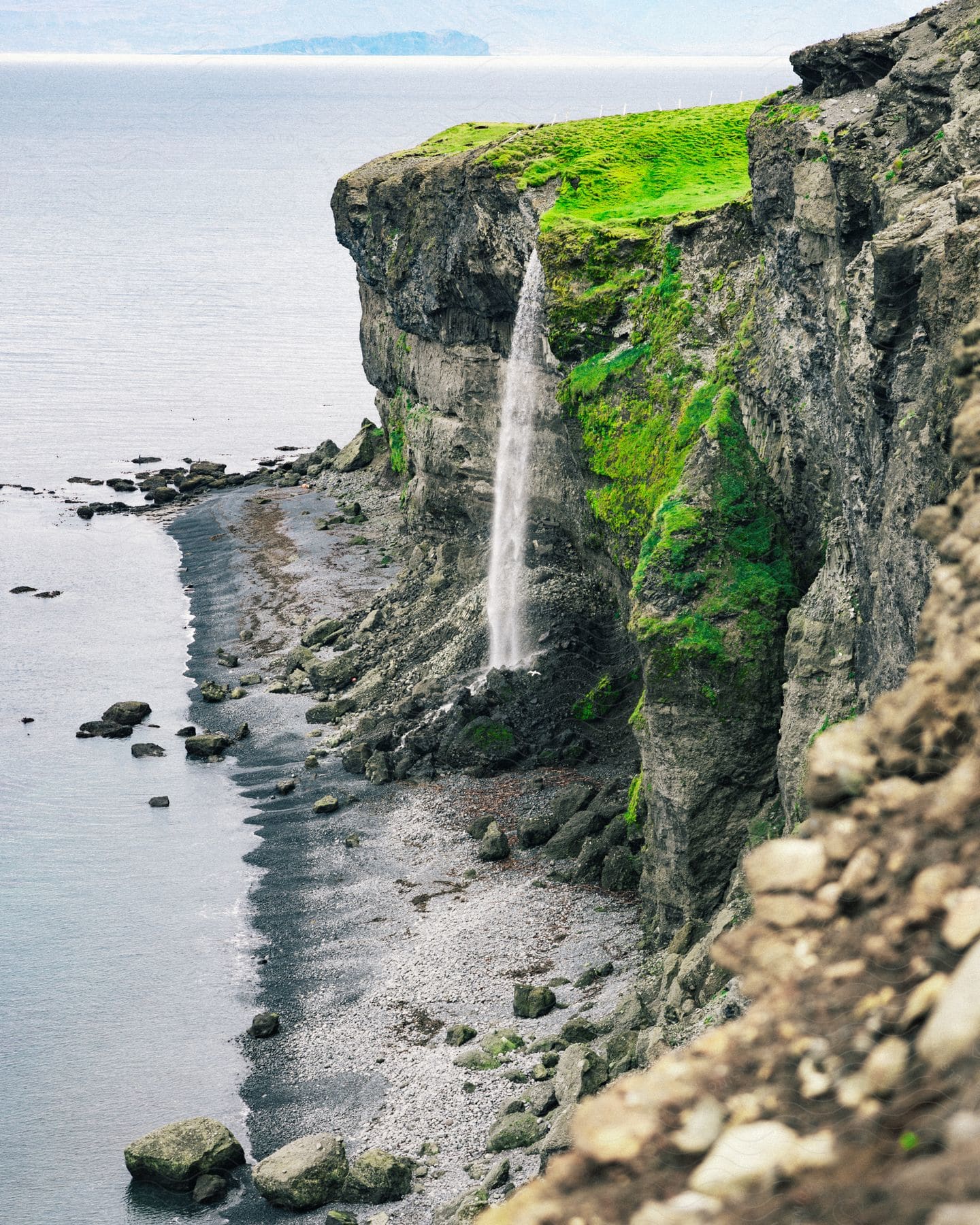 an island with a cliff causing a water fall near the calm ocean