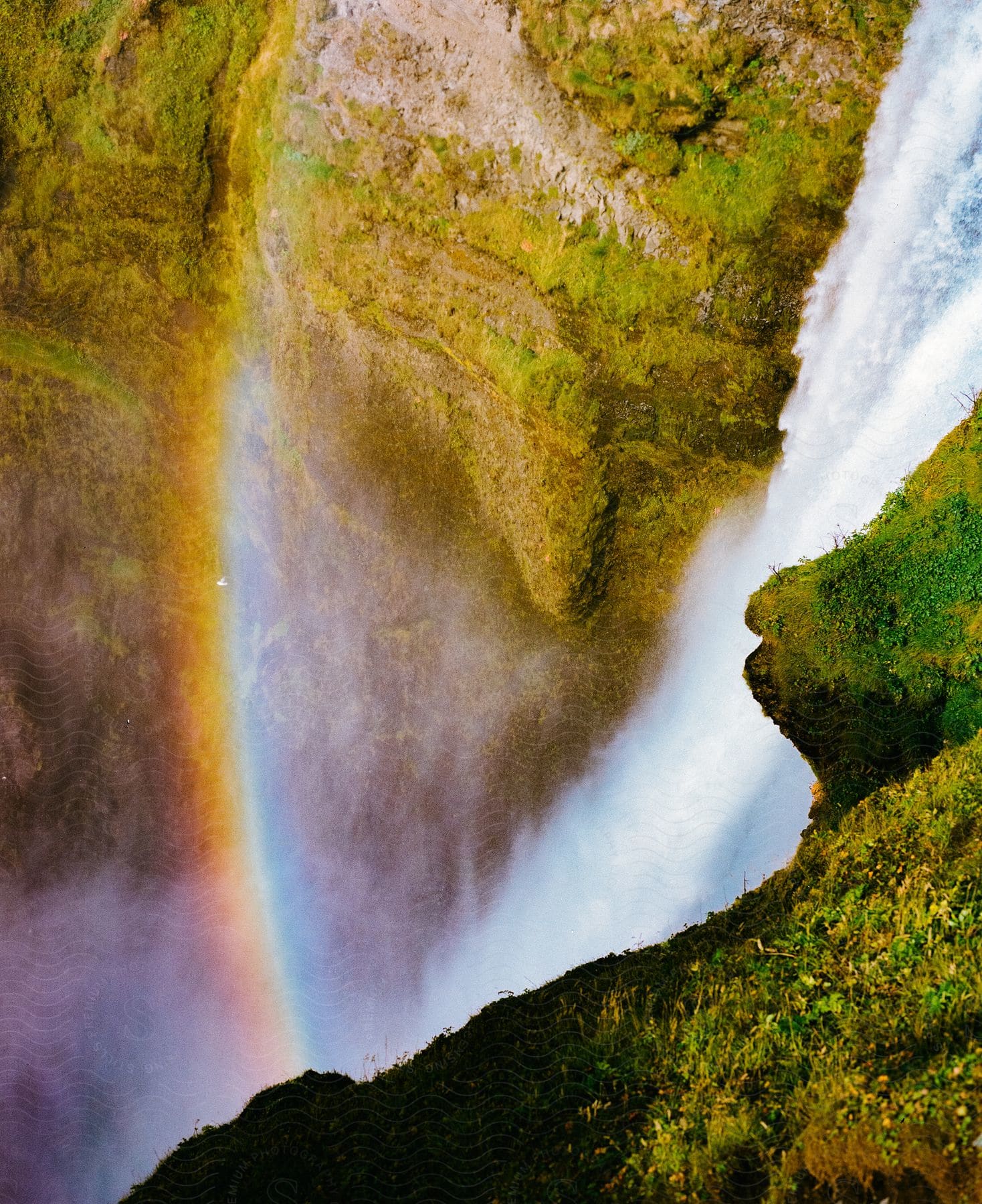 A rainbow forms next to a waterfall that pours over a steep cliffside.