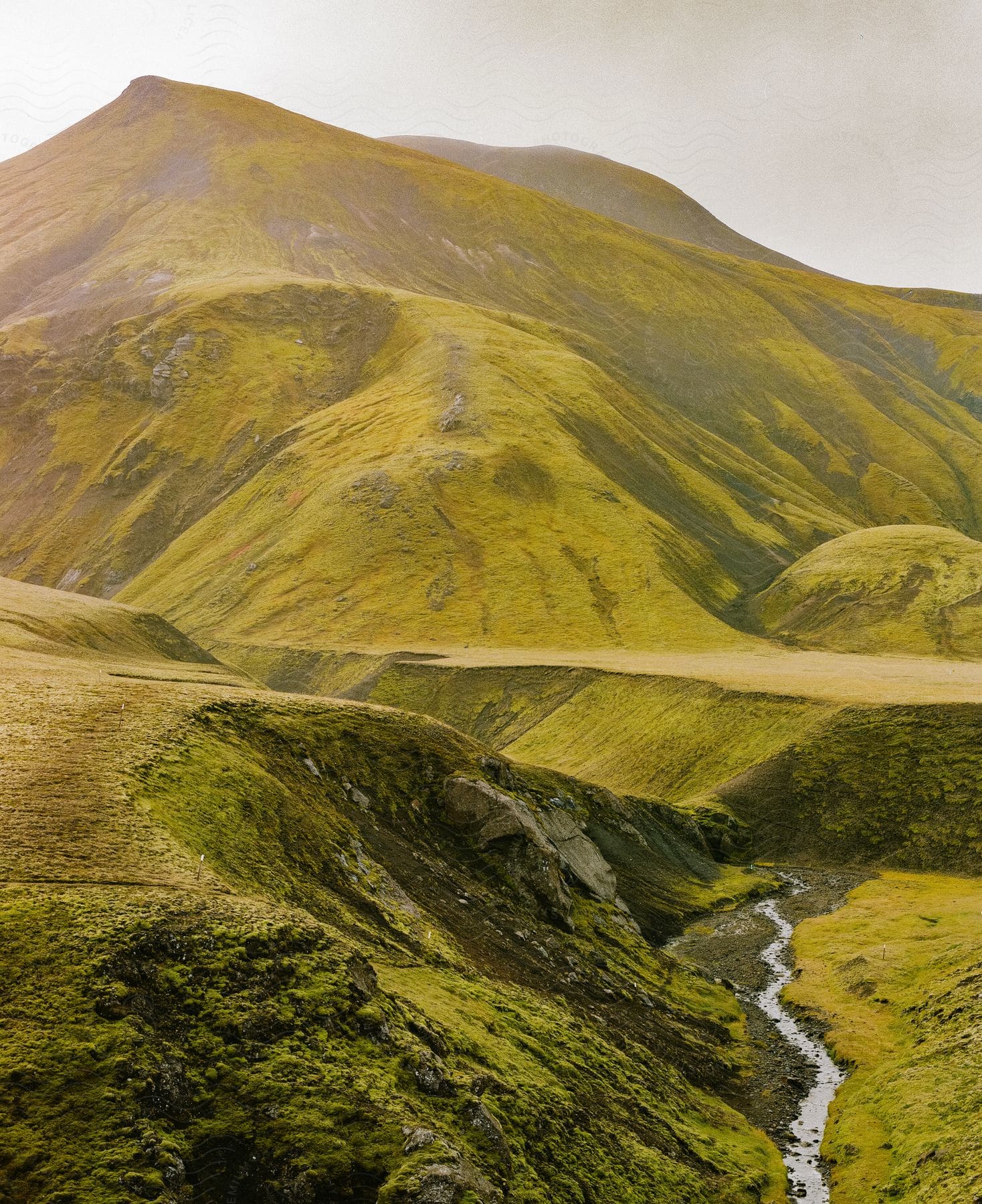 A stream winds through a canyon below green covered hills and mountains