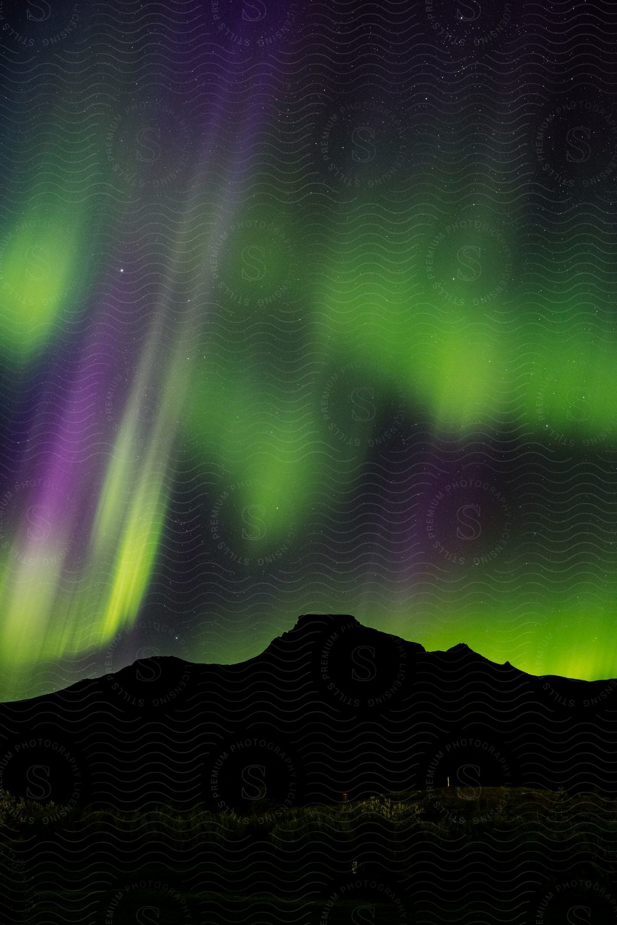 Green and purple Northern Lights glow over mountains in the night sky