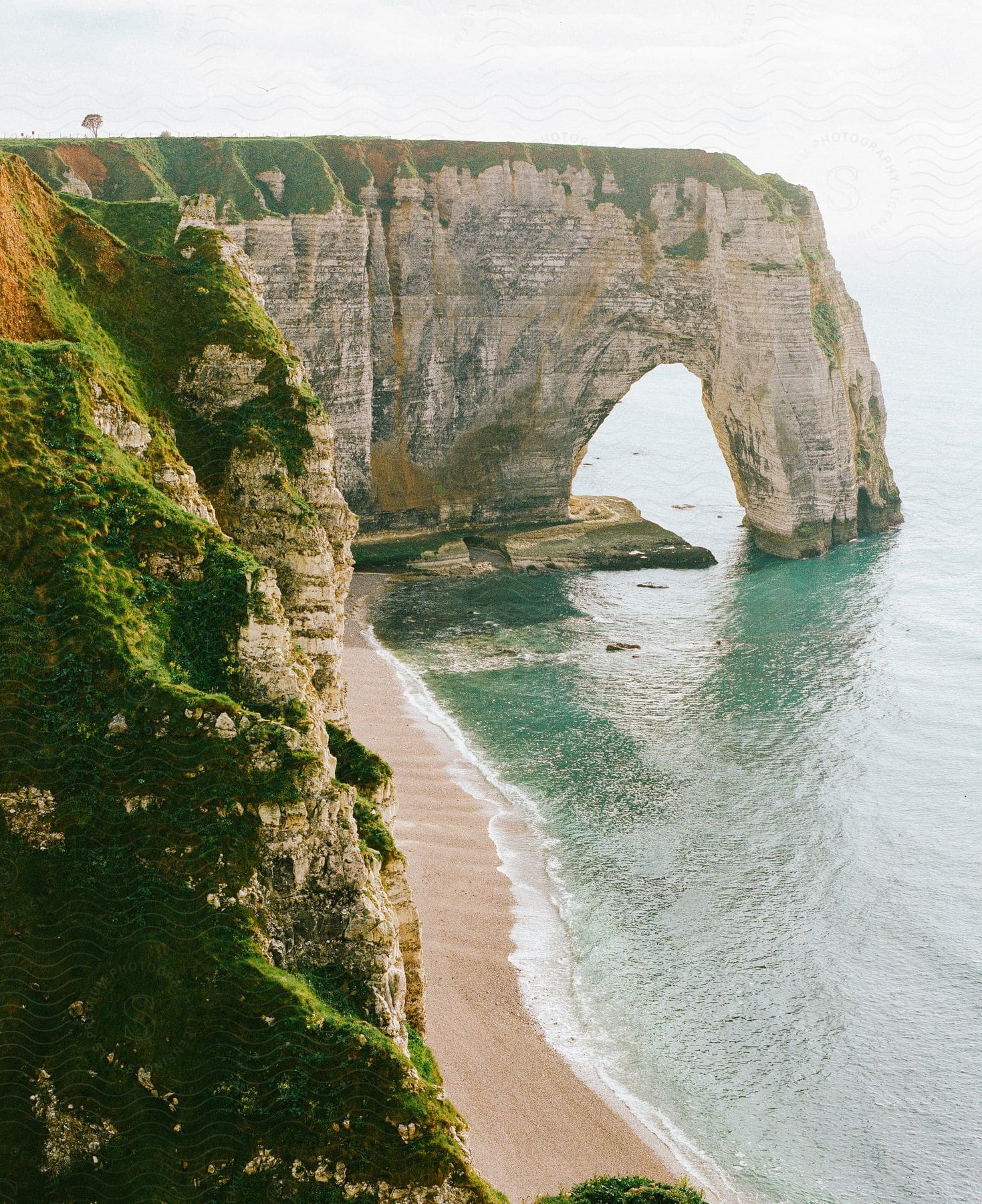 An arched rock formation off a coastal cliff as waves roll into shore and over the beach