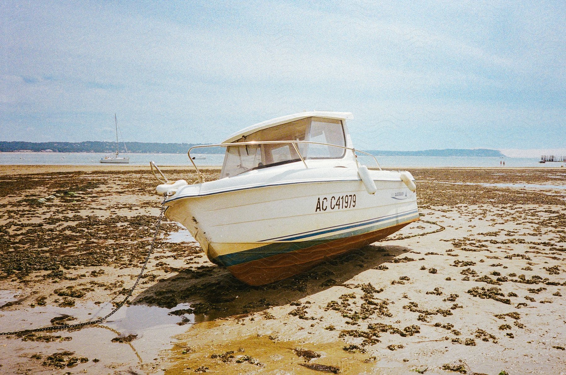 A boat sits on shore as another boat sails off the coast