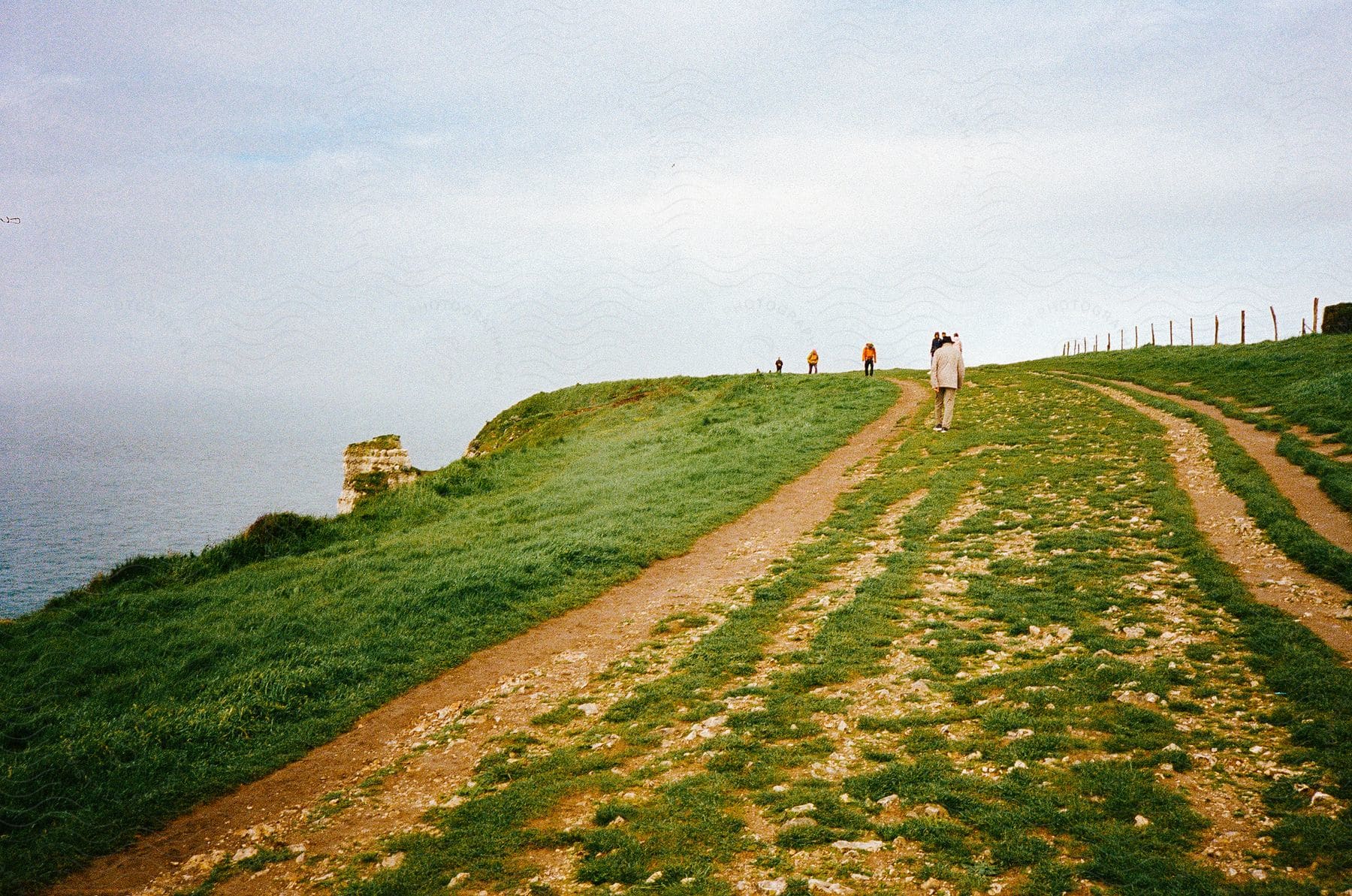 People are walking up a hill overlooking the coast under a cloudy sky