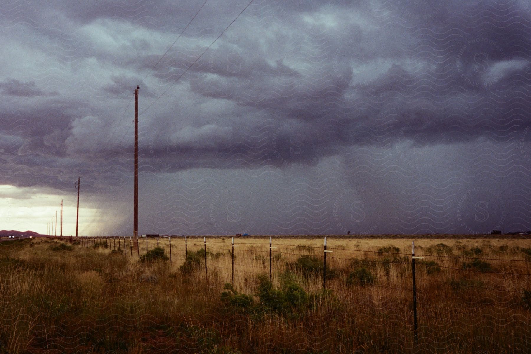 A heavy rain storm moving across a field toward powerlines and road