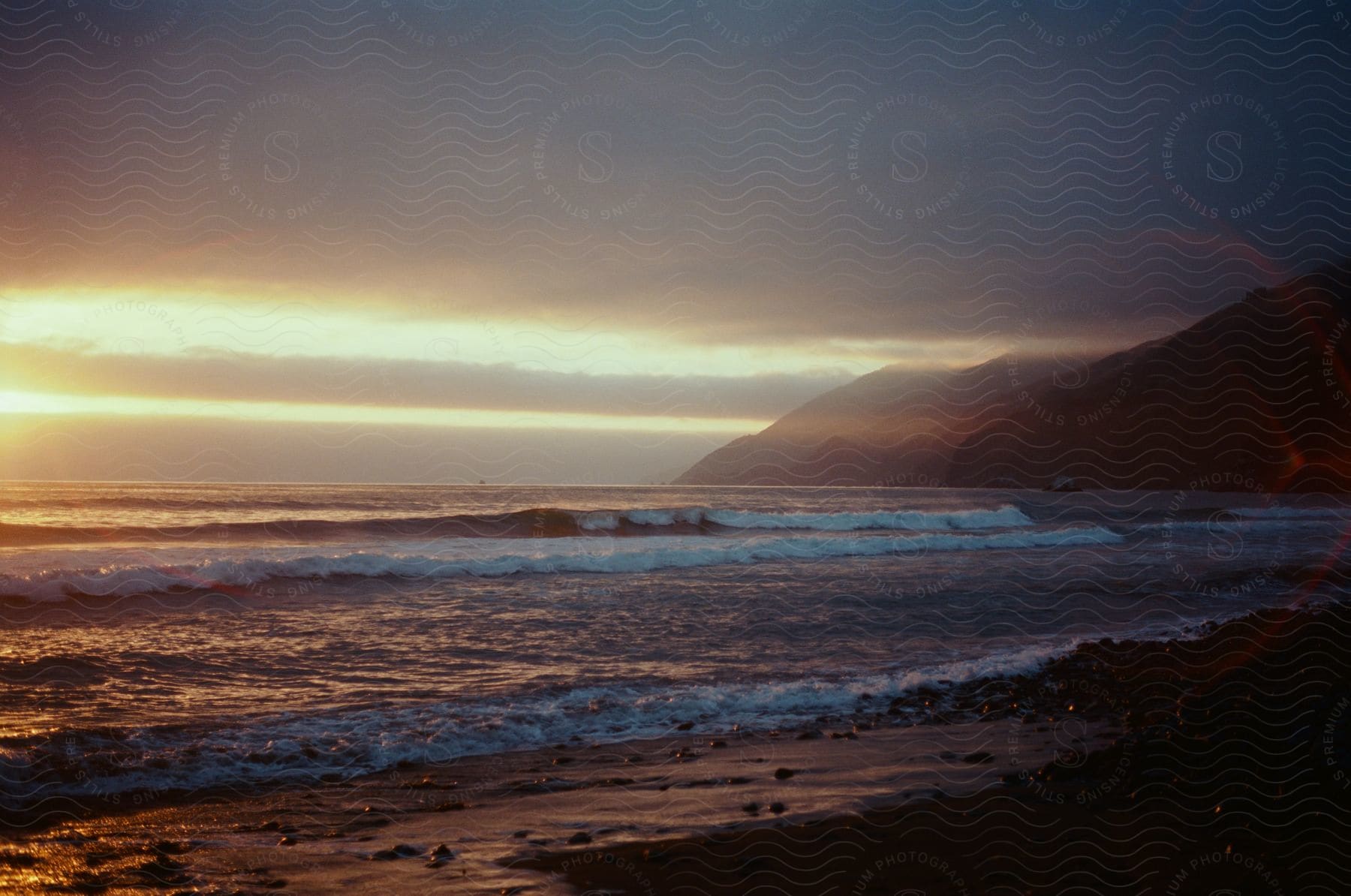 Ocean waves curling and breaking as they come to shore on a beach near coastal hills