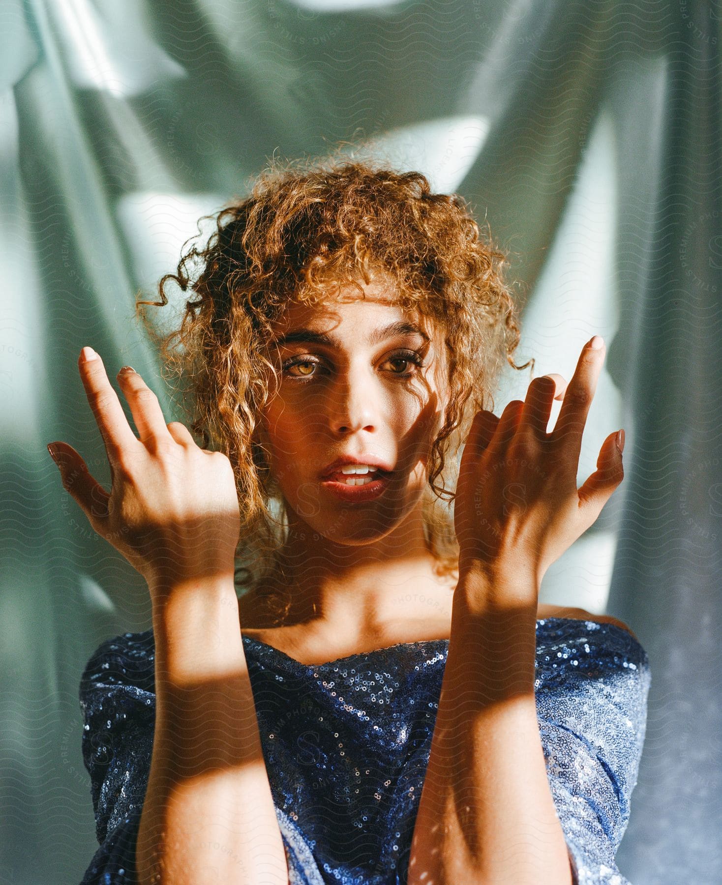 A portrait of a woman standing in the sunlight in front of a curtain.