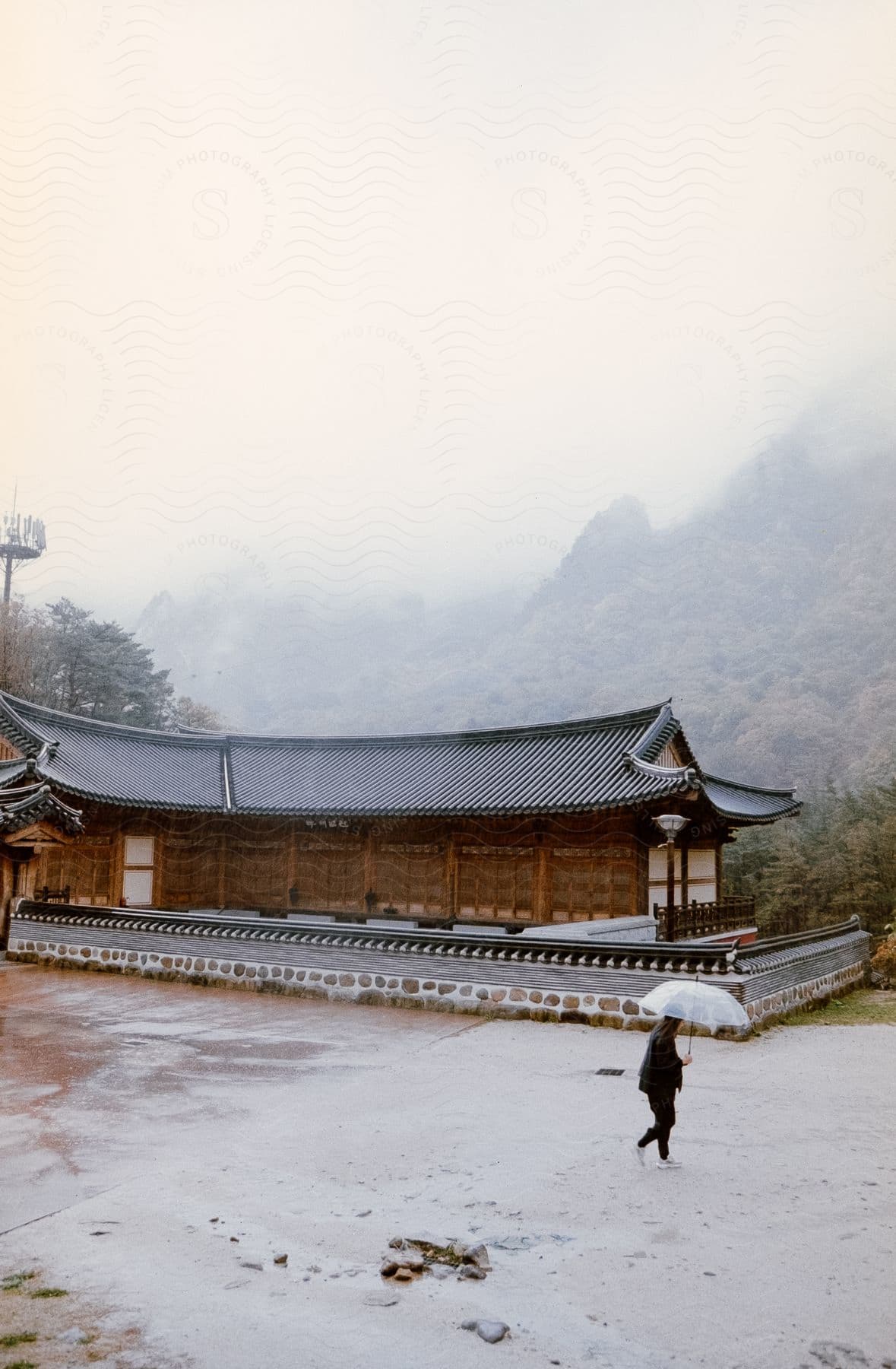 View Of An Asian-style Wooden House Amidst A Hill By The Mountains On A Misty Day