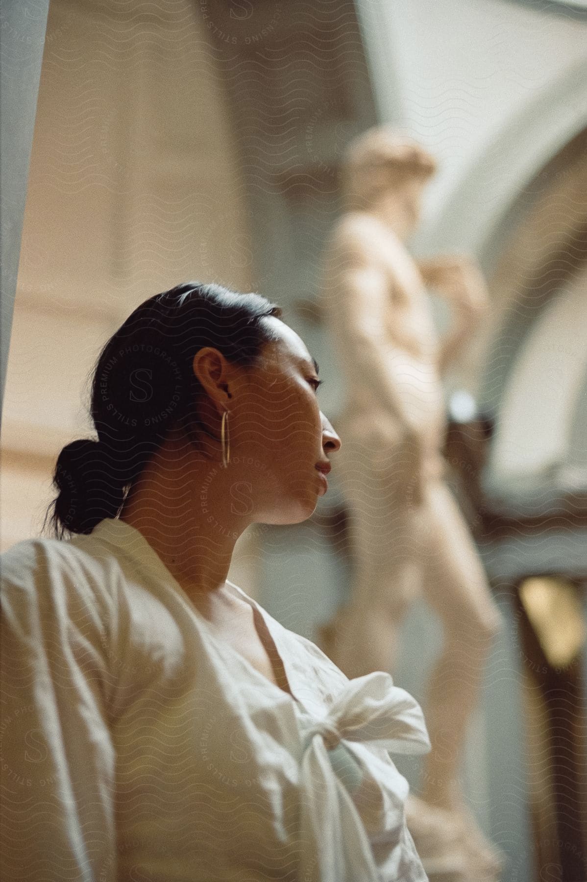 Side view of the upper body of a woman wearing a white top with black hair tied up.