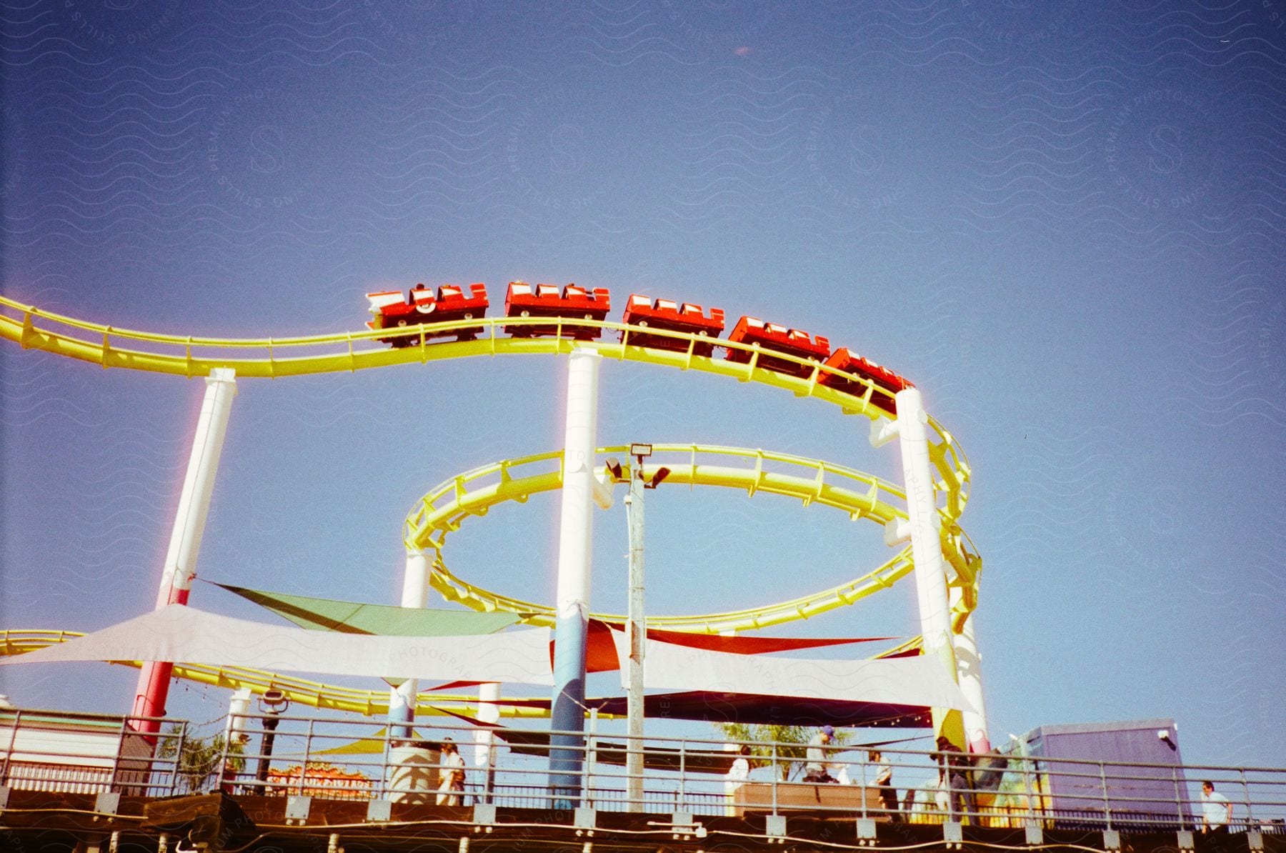 A group of red cars sits on a yellow rollercoaster track on a sunny, summer day.