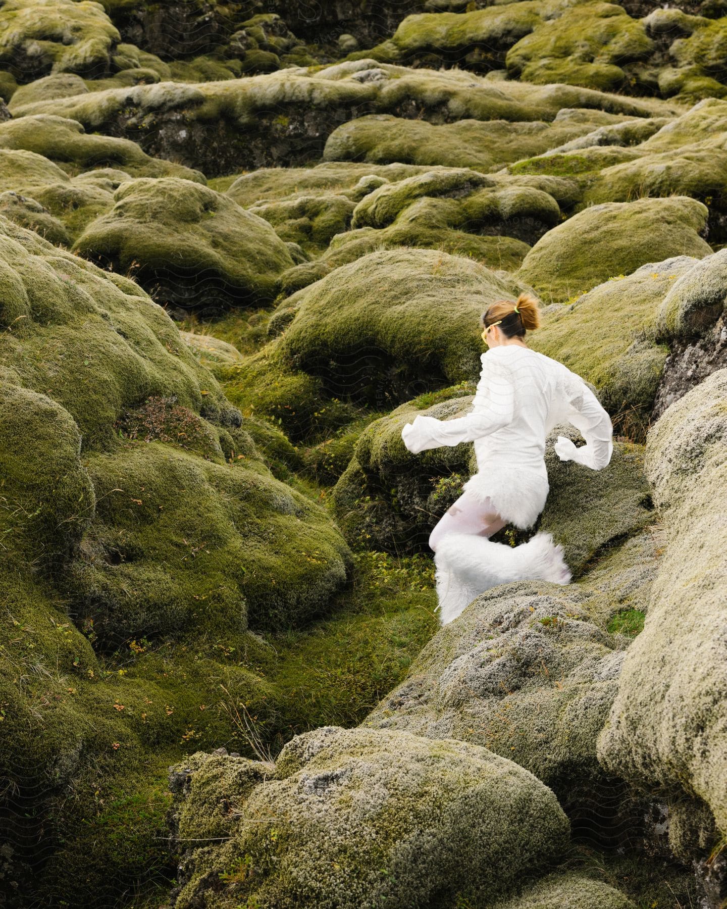 A woman wearing white clothes runs on a moss covered mountainside