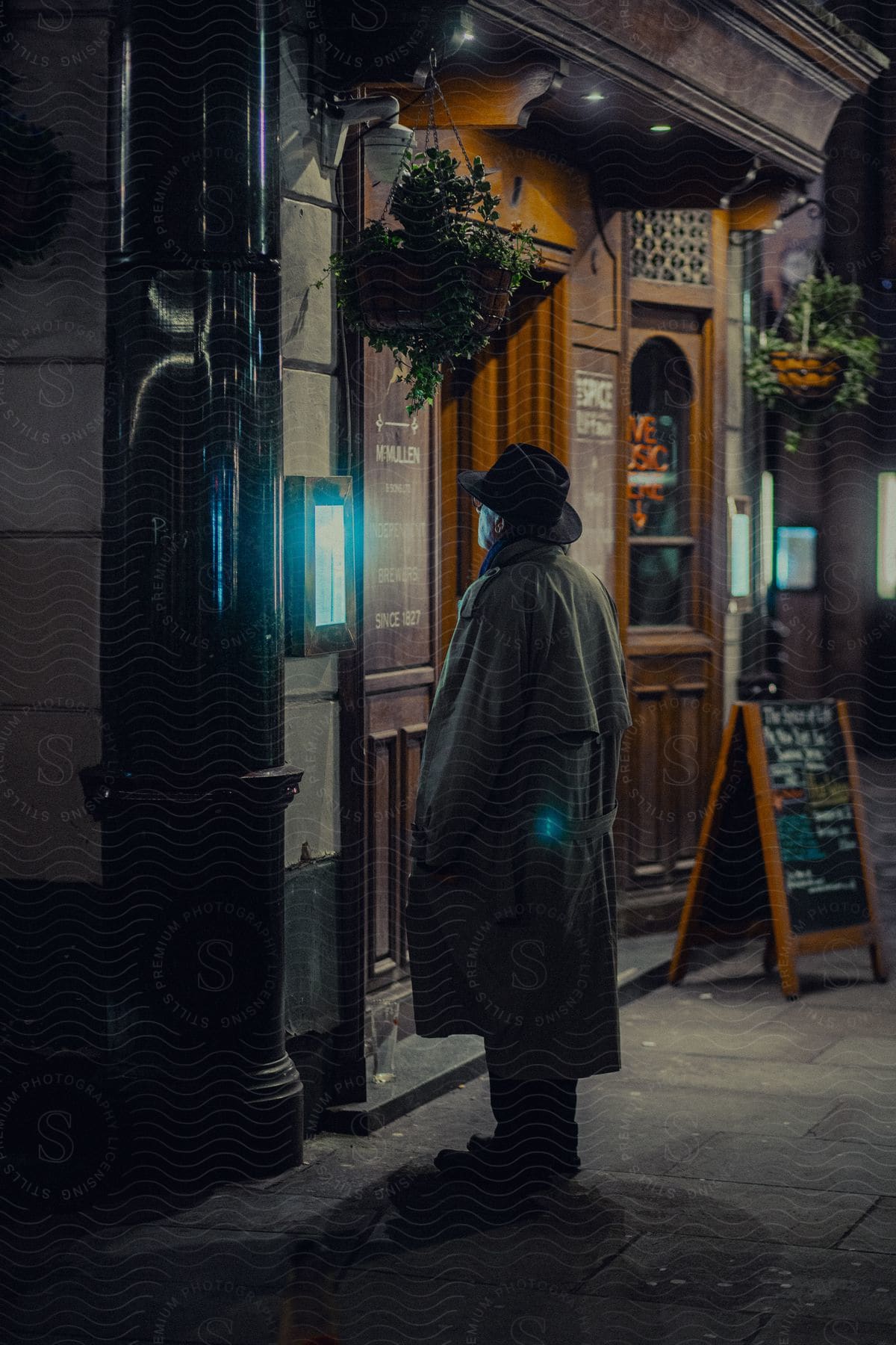 A man wearing a trench coat and hat stands outside a McMullens pub reading the menu on display