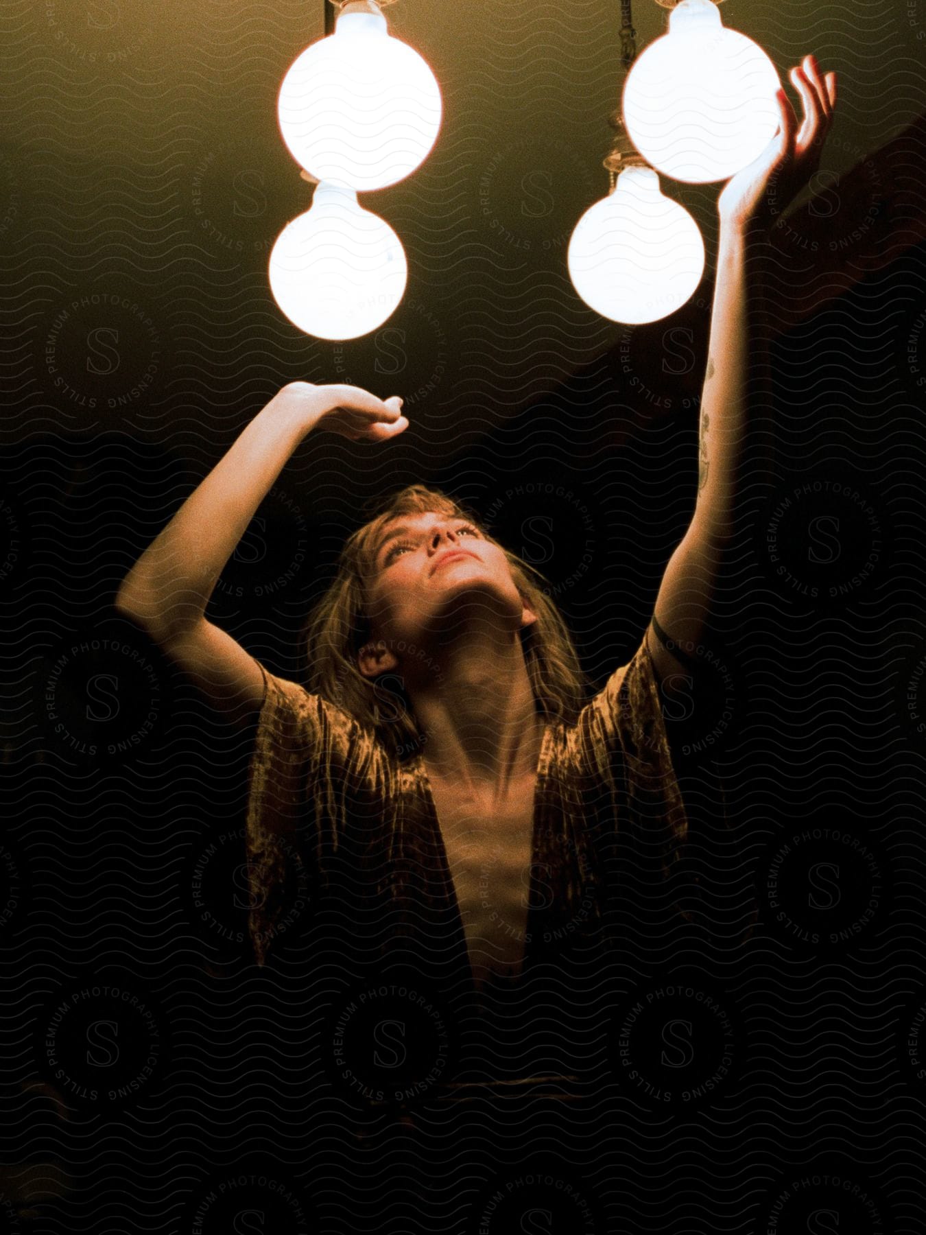 A woman is dancing in a room as she raises her hands to the lights