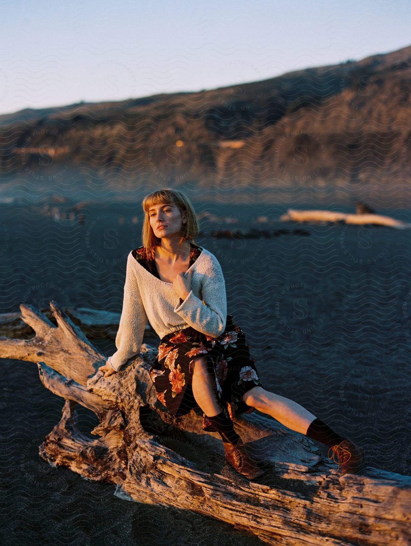 Fashion model sits on large piece of driftwood at the beach.