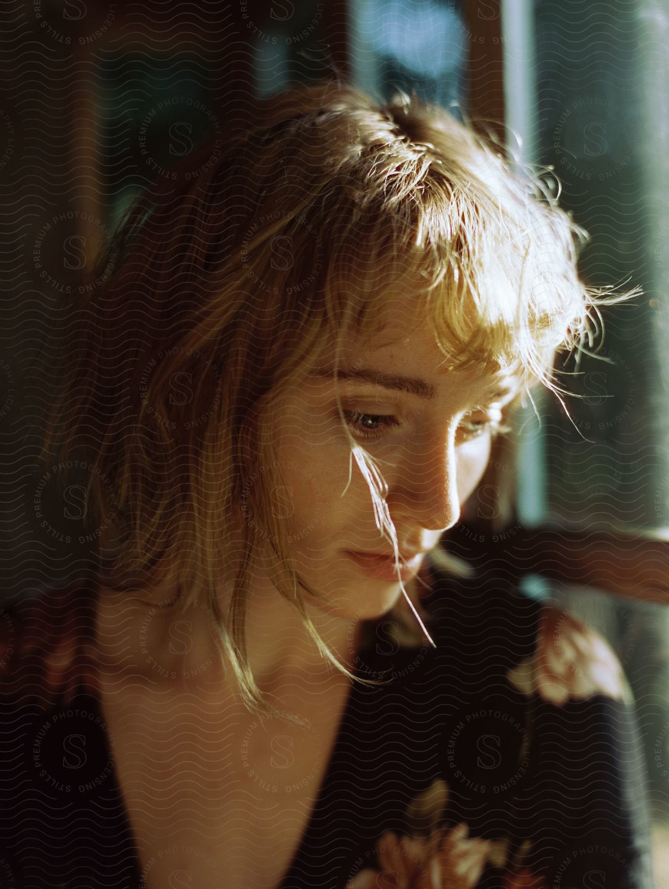 A woman sitting near a window looking down with sunlight shining on her hair