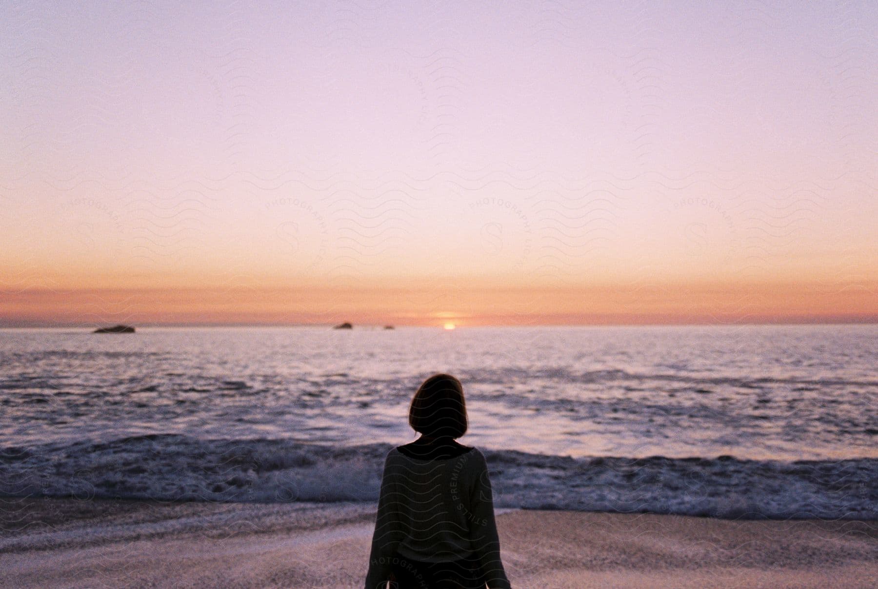 Person stands in silhouette on the beach gazing at the pink sunset on horizon