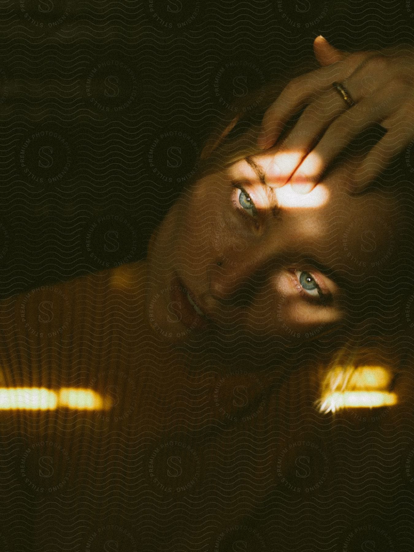 Close-up of a woman in a yellow sweater, hand on forehead, with sunlight casting shadows across her face.