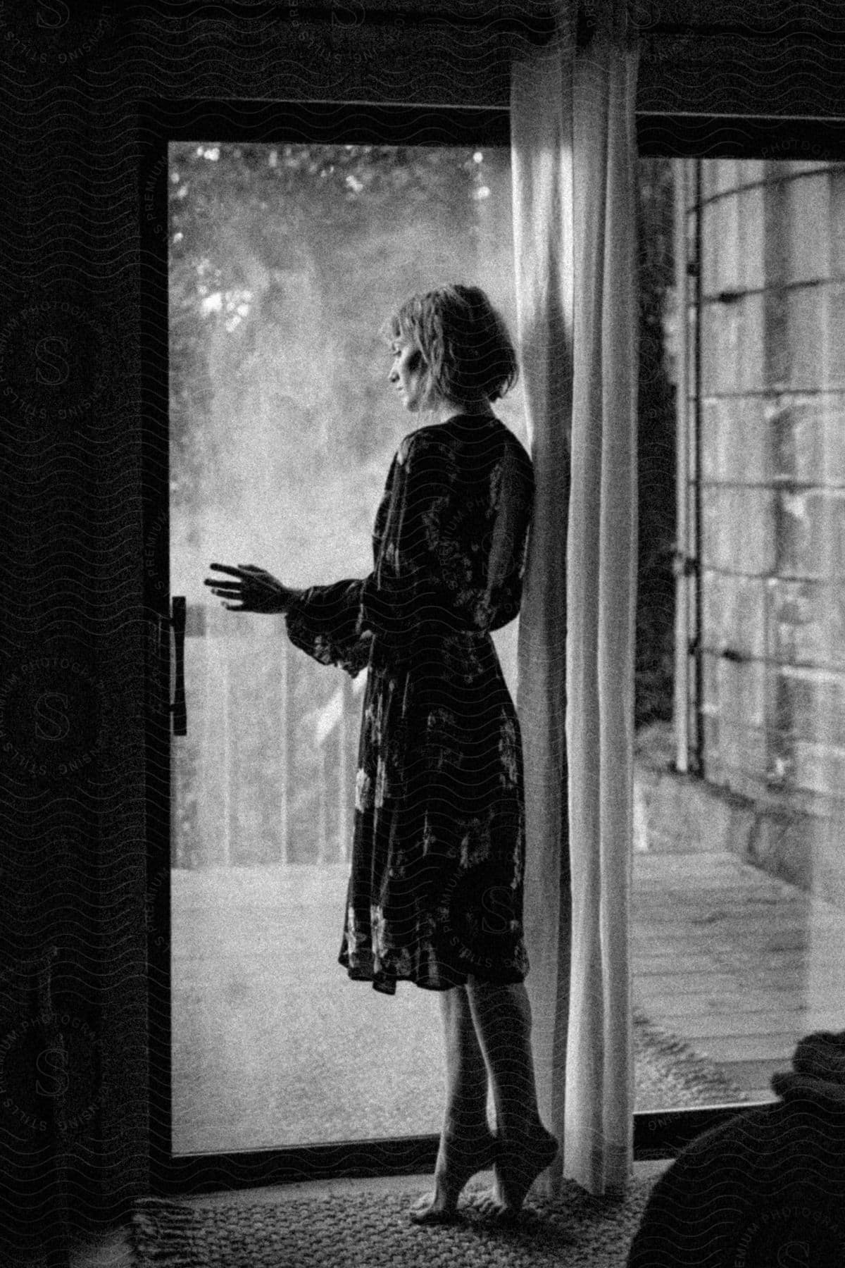 Woman wearing midi dress poses looking out sliding door window