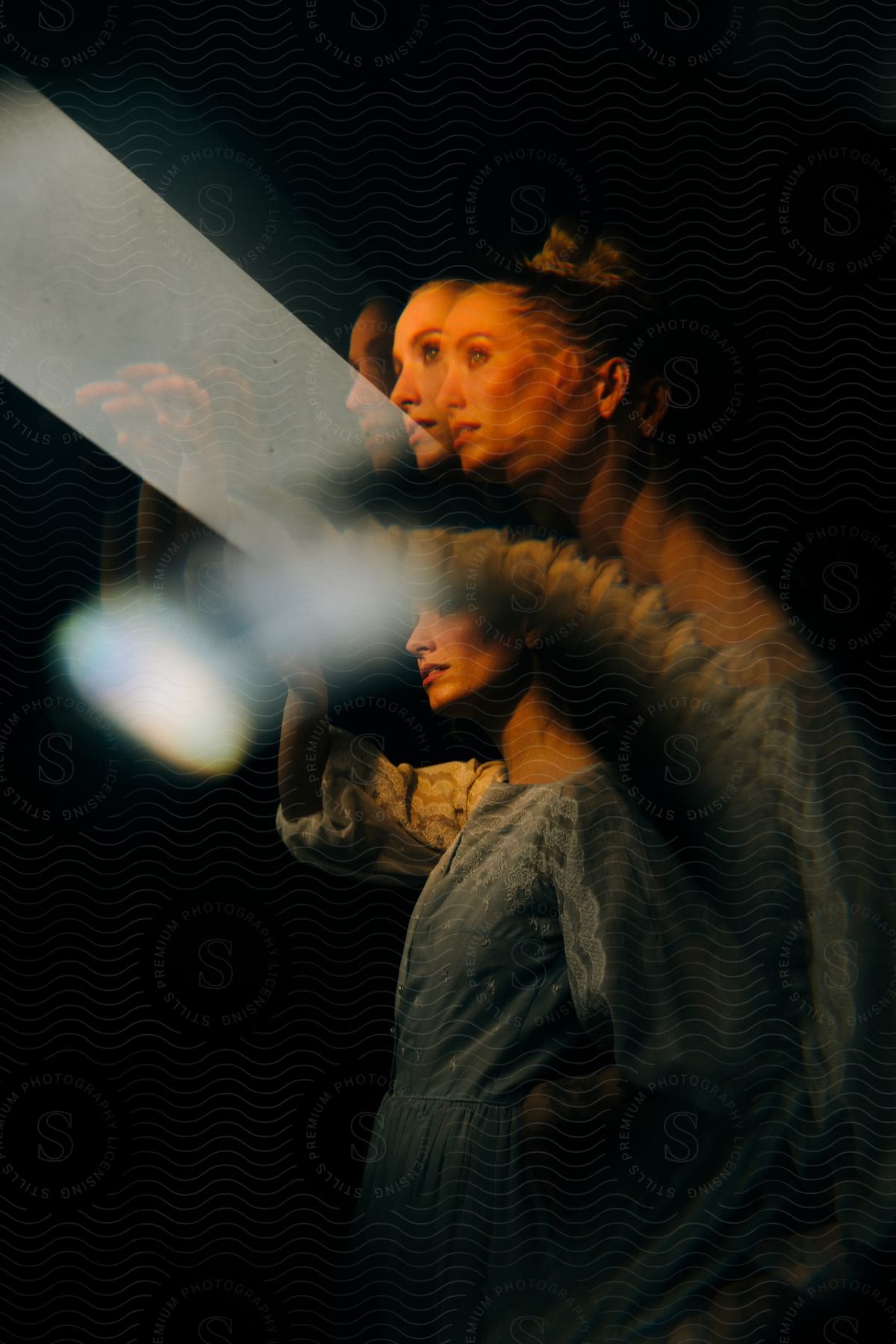 Multiple exposures of a woman in a long blue dress in a dark room.