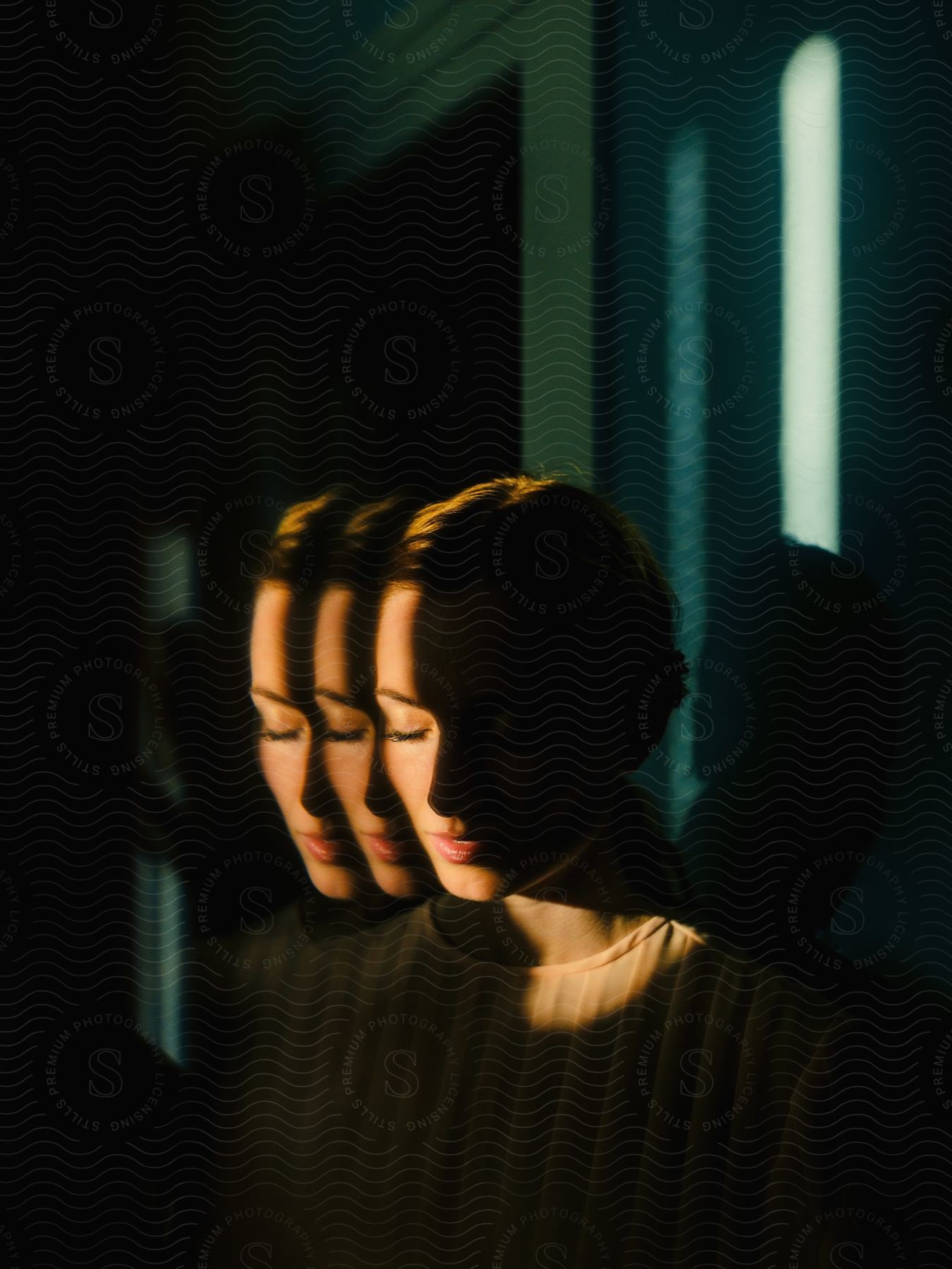 Light illuminates part of face of woman standing in shadowed room.