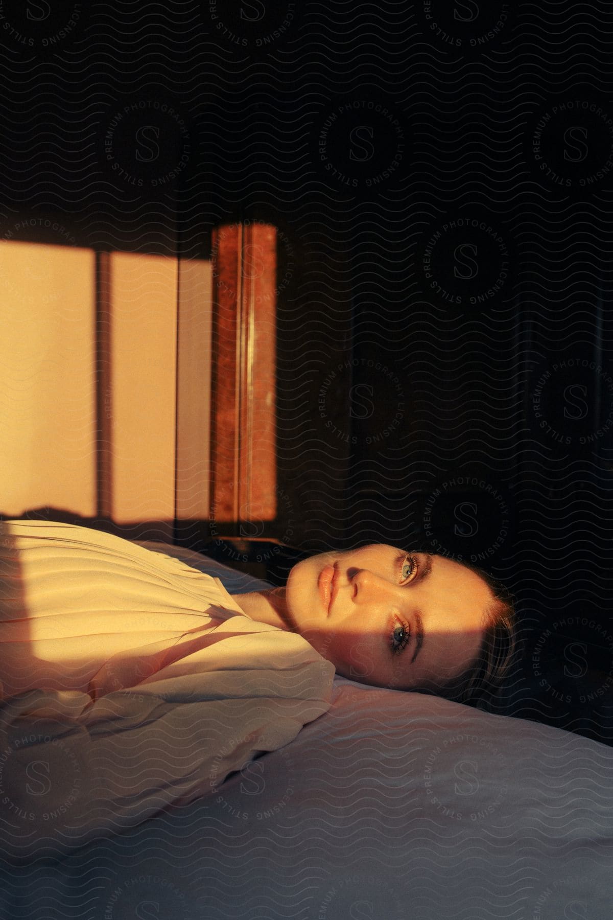 Portrait of a young woman with light eyes lying on the bed with sunlight reflection.