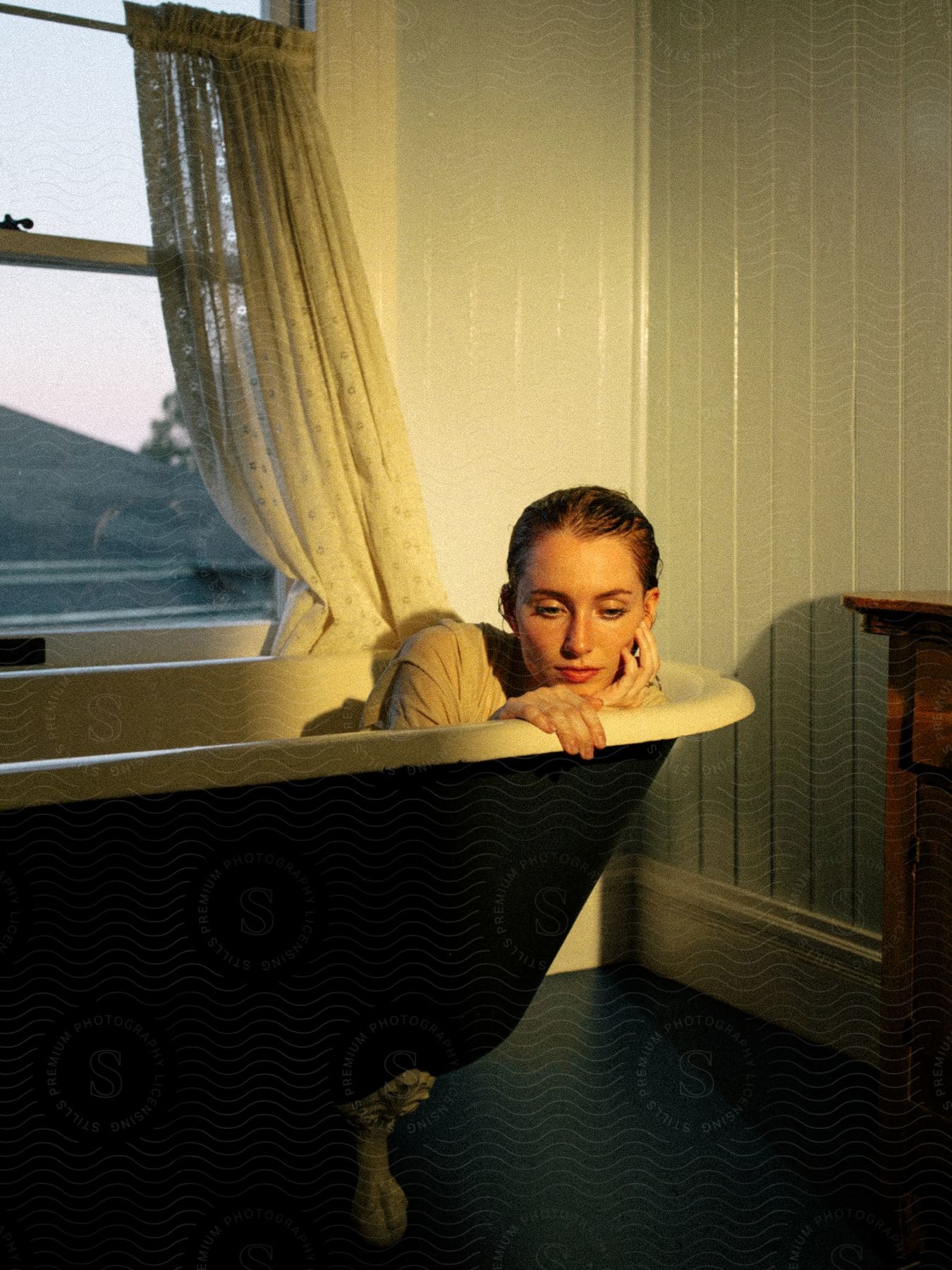 Woman in clothing modeling with wet hair inside a vintage bathtub.