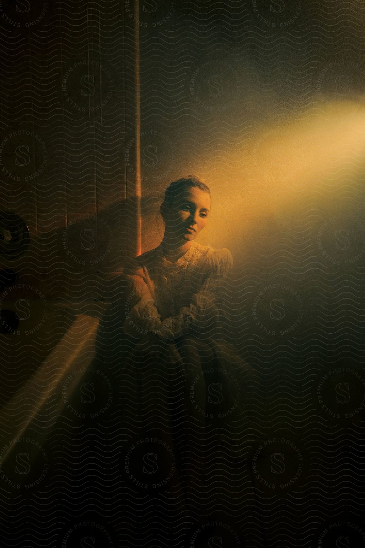 Woman wearing fashionable dress sits on floor in dimly lit bathroom.