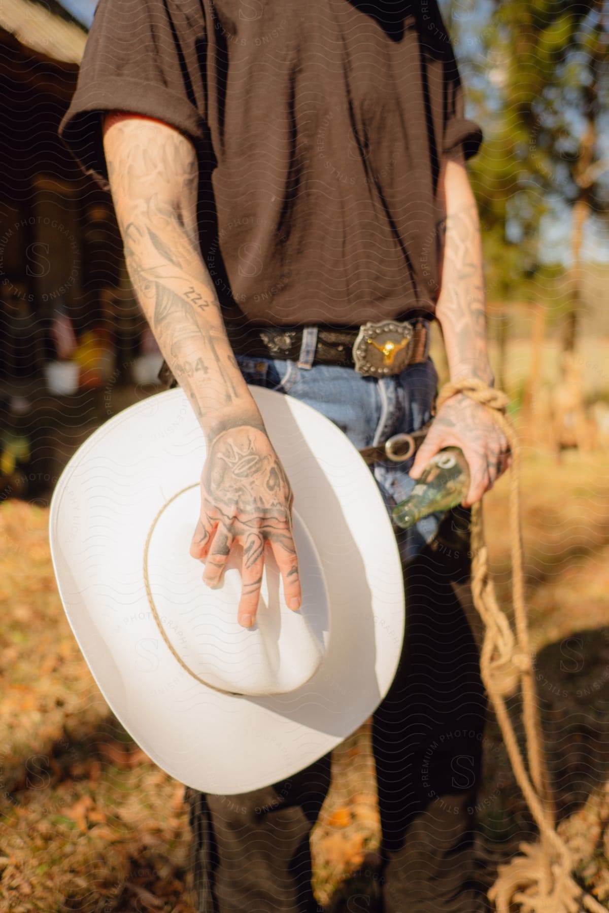 A man with tattoos on his hands and arms holds a white cowboy hat to his side