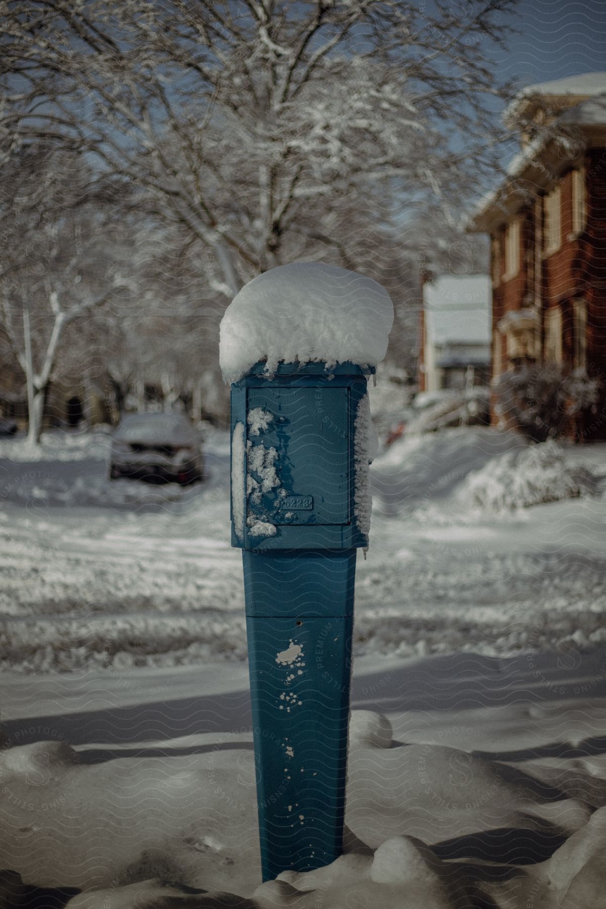 A skinny blue mailbox with snow on top.