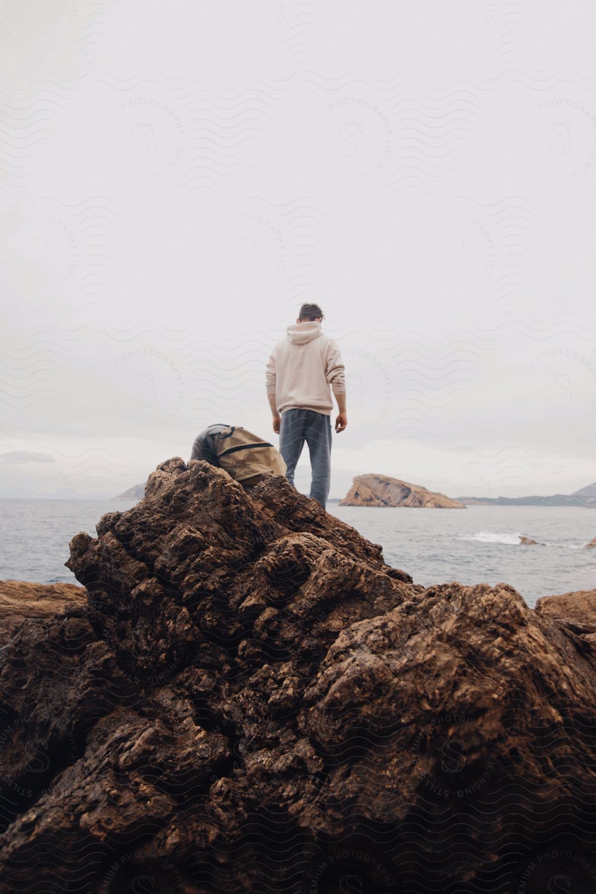 a man wearing a hoody standing on a rock by the sea looking at the waters