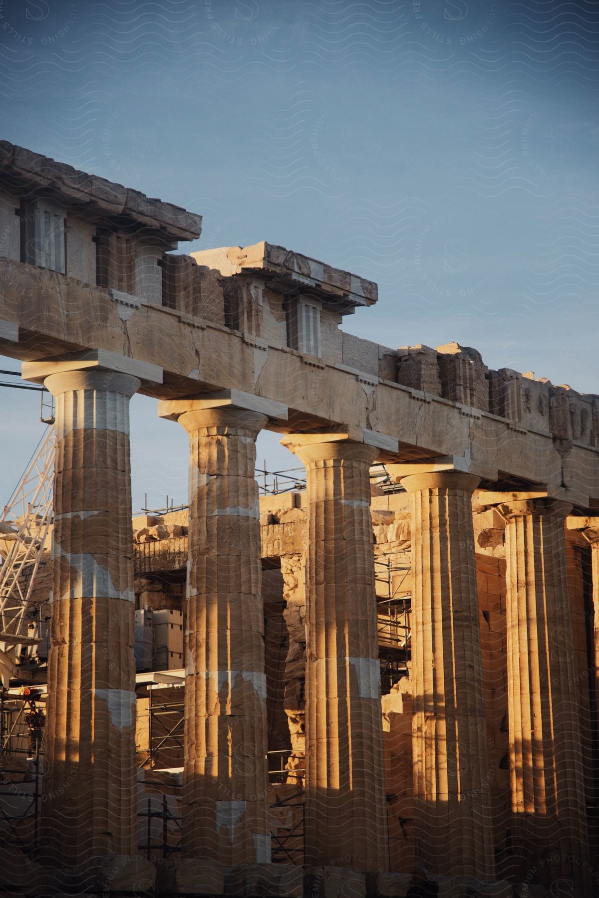 Ancient columns of a historical structure bathed in the light of the setting sun, with scaffolding of restoration work.