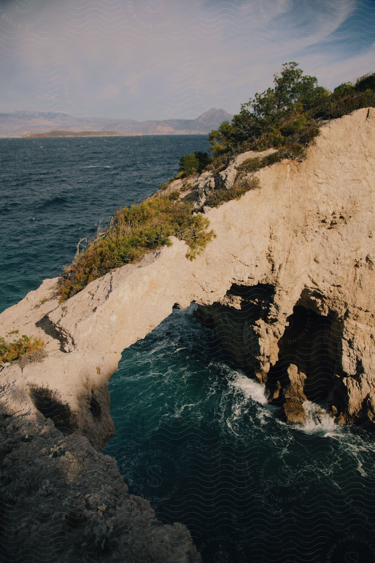 Water flows under a stone arch along the coast with mountains in the distance