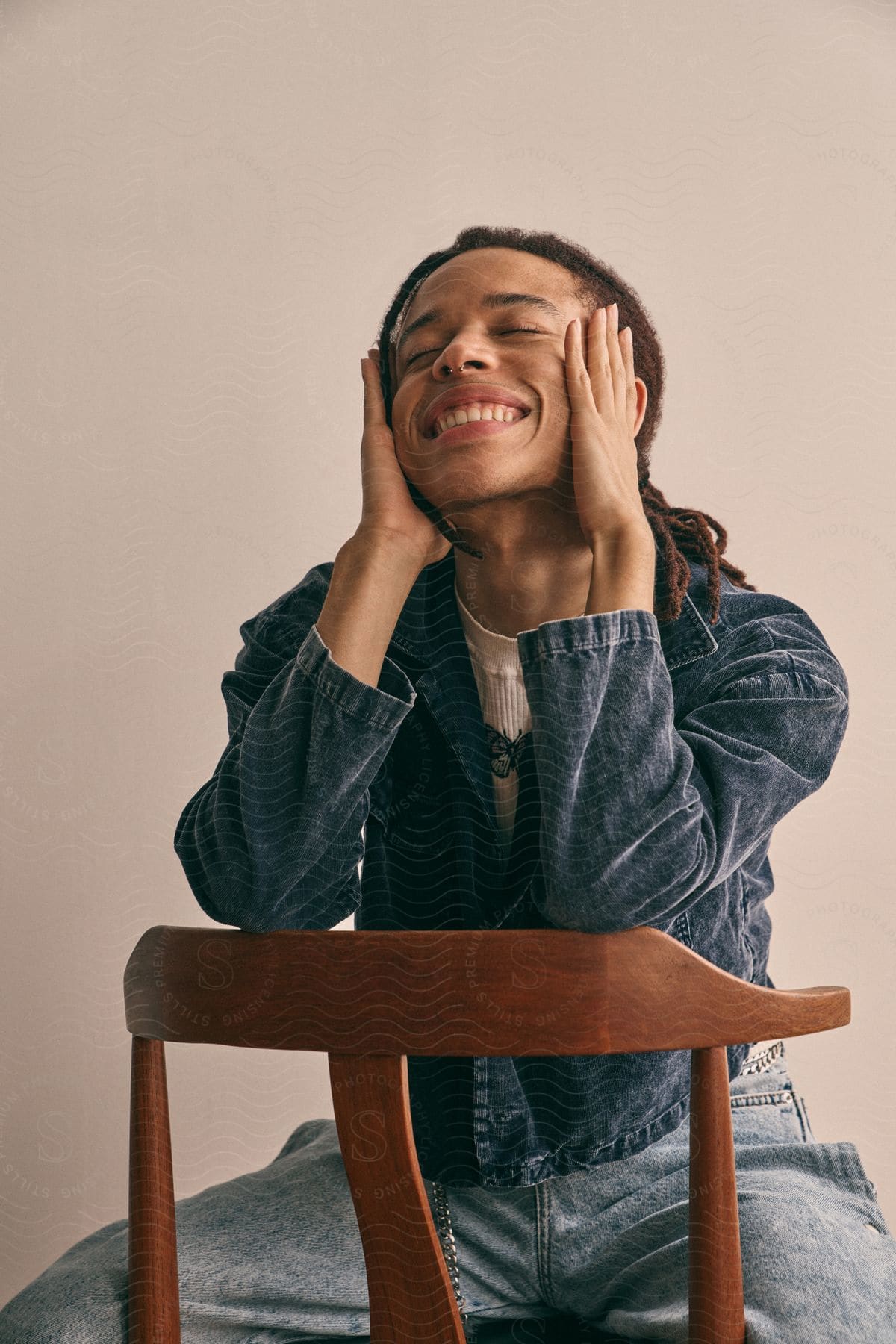 Man with dreadlocks sitting in a chair, sculpting, smiling, and wearing denim clothes.