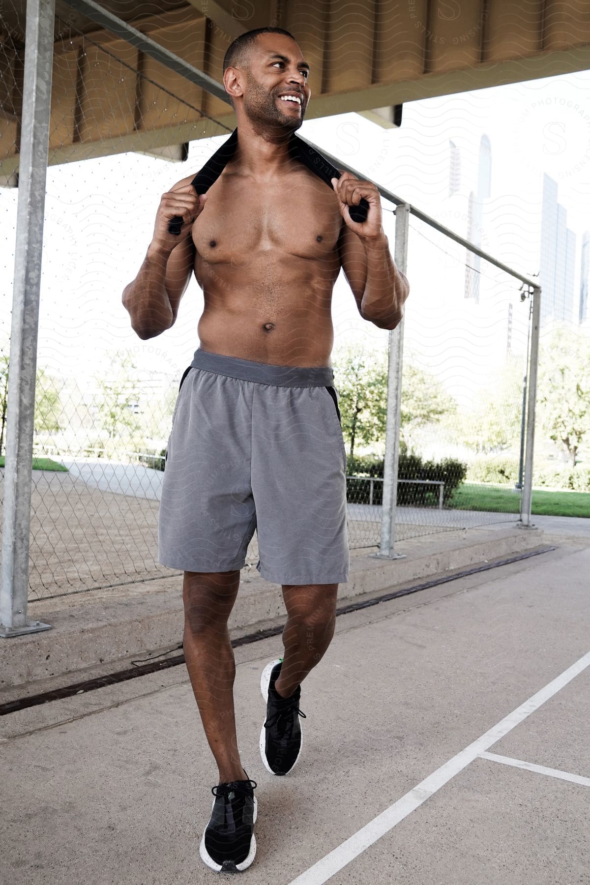 A muscled man in shorts and no shirt walks into a sports area smiling.