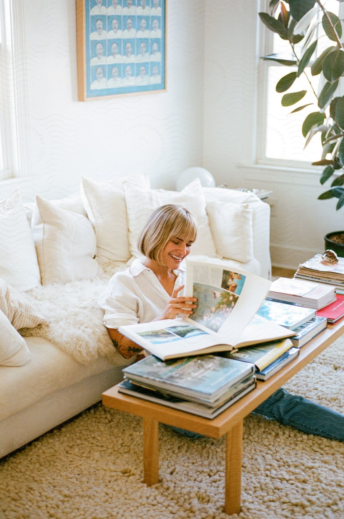 A woman sitting on the floor in front of her couch, going through coffee table books on her coffee table