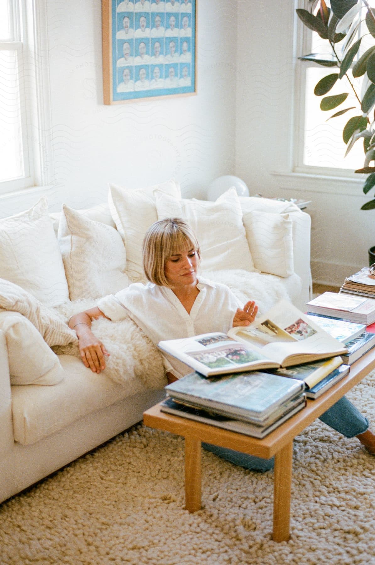 Interior design of a room with a white sofa and a woman sitting on the floor reading a book.