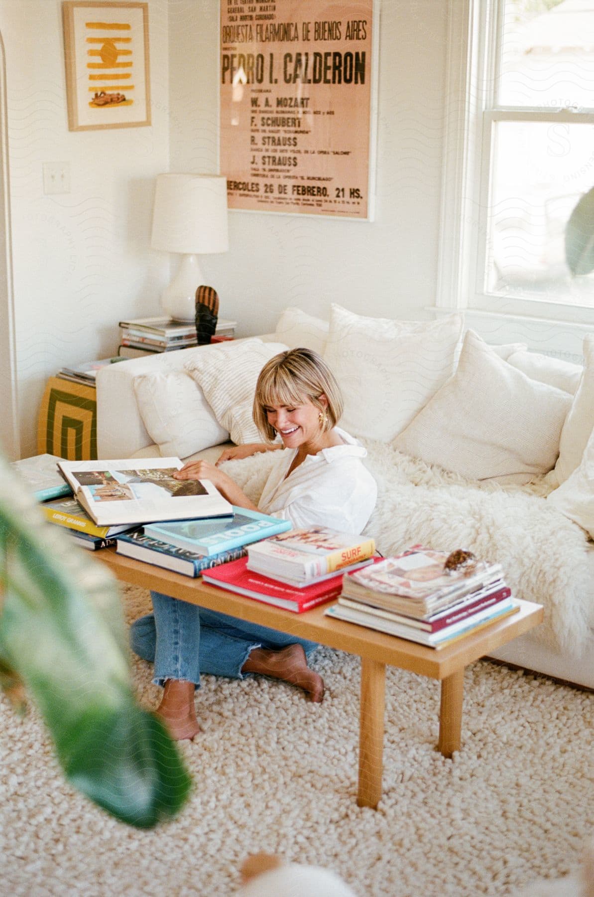 A woman sitting on the floor in front of her couch, going through the coffee table books on her coffee table.