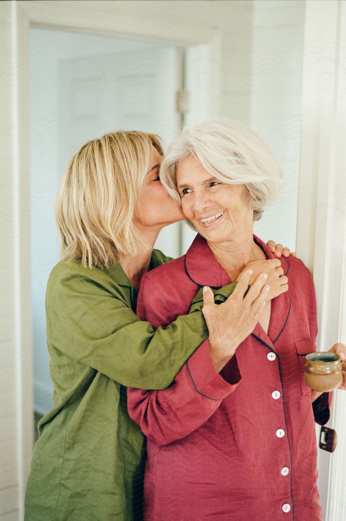 A woman is kissing another on the cheek while both wear pajamas