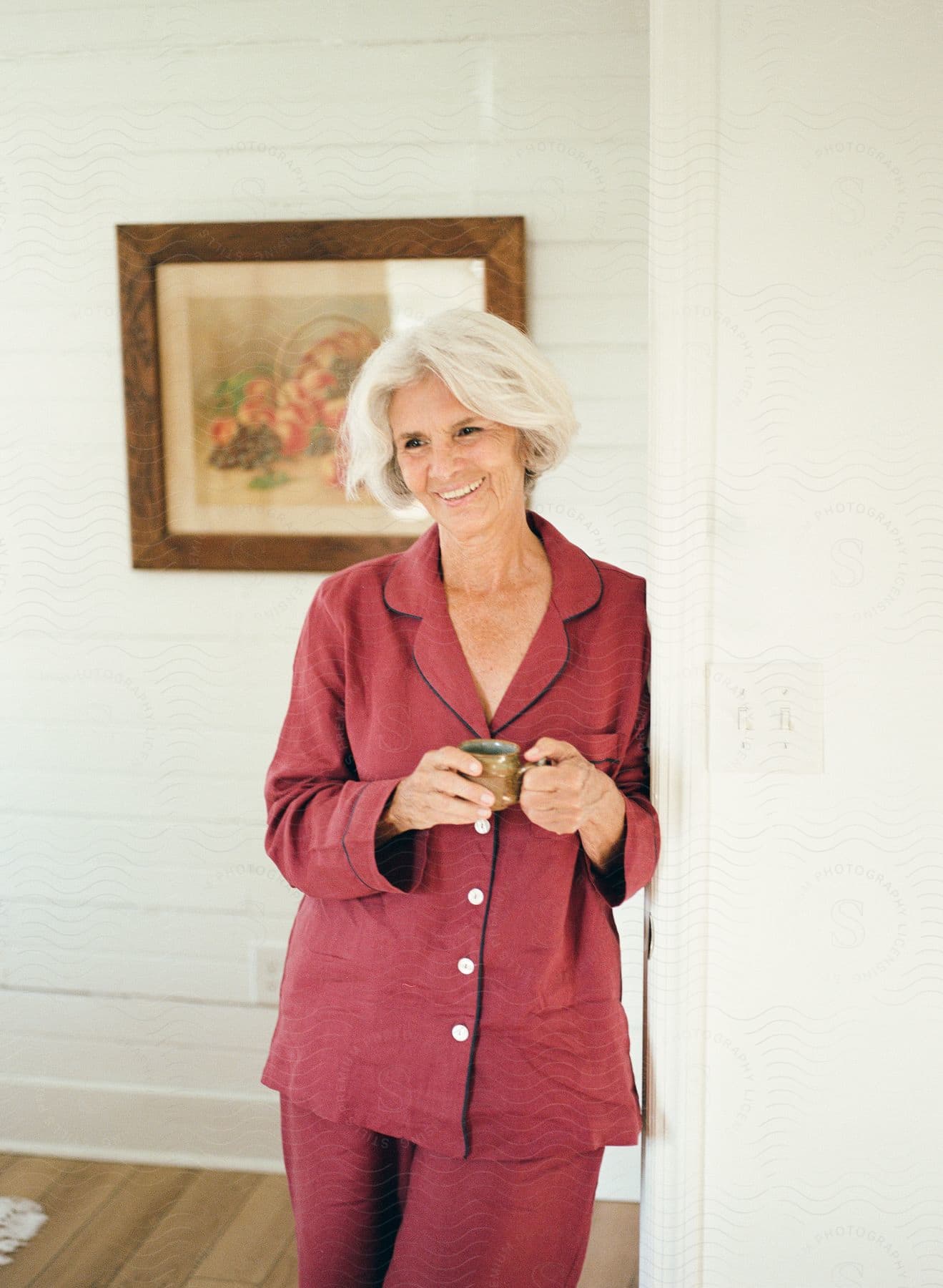 Lady standing indoors wearing red buttoned pajamas and holding a cup.