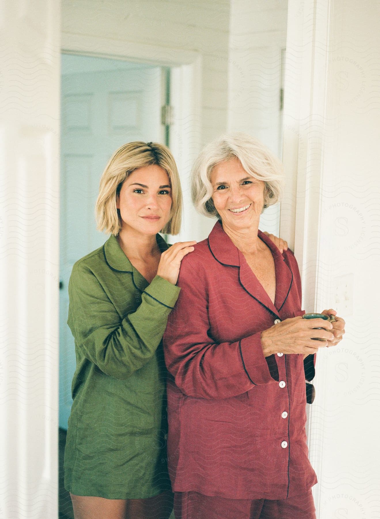 Two people with smiling faces are standing next to each other indoors. One person is wearing an olive green shirt and the other is wearing a red shirt with buttons down the front.