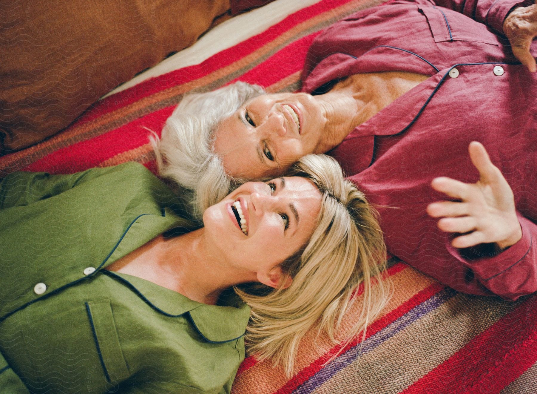 A smiling mother and daughter lying down on a striped blanket.