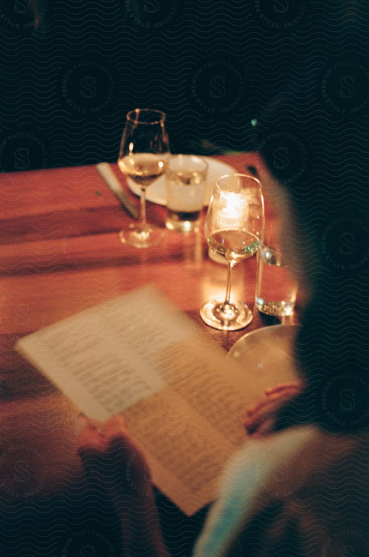 Glasses of wine are on a restaurant table as a woman reads the menu