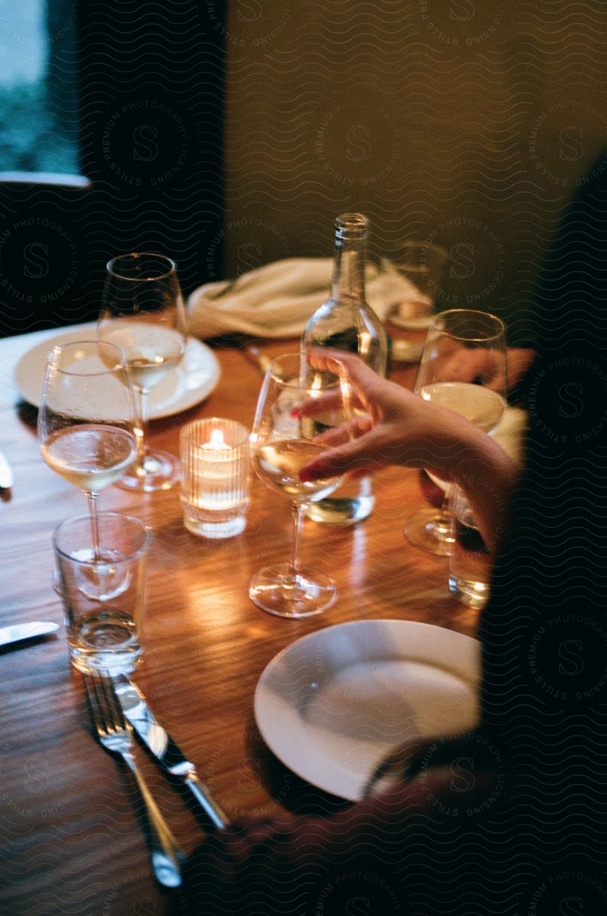 Woman sitting at a table with glasses, cutlery, and white wine.