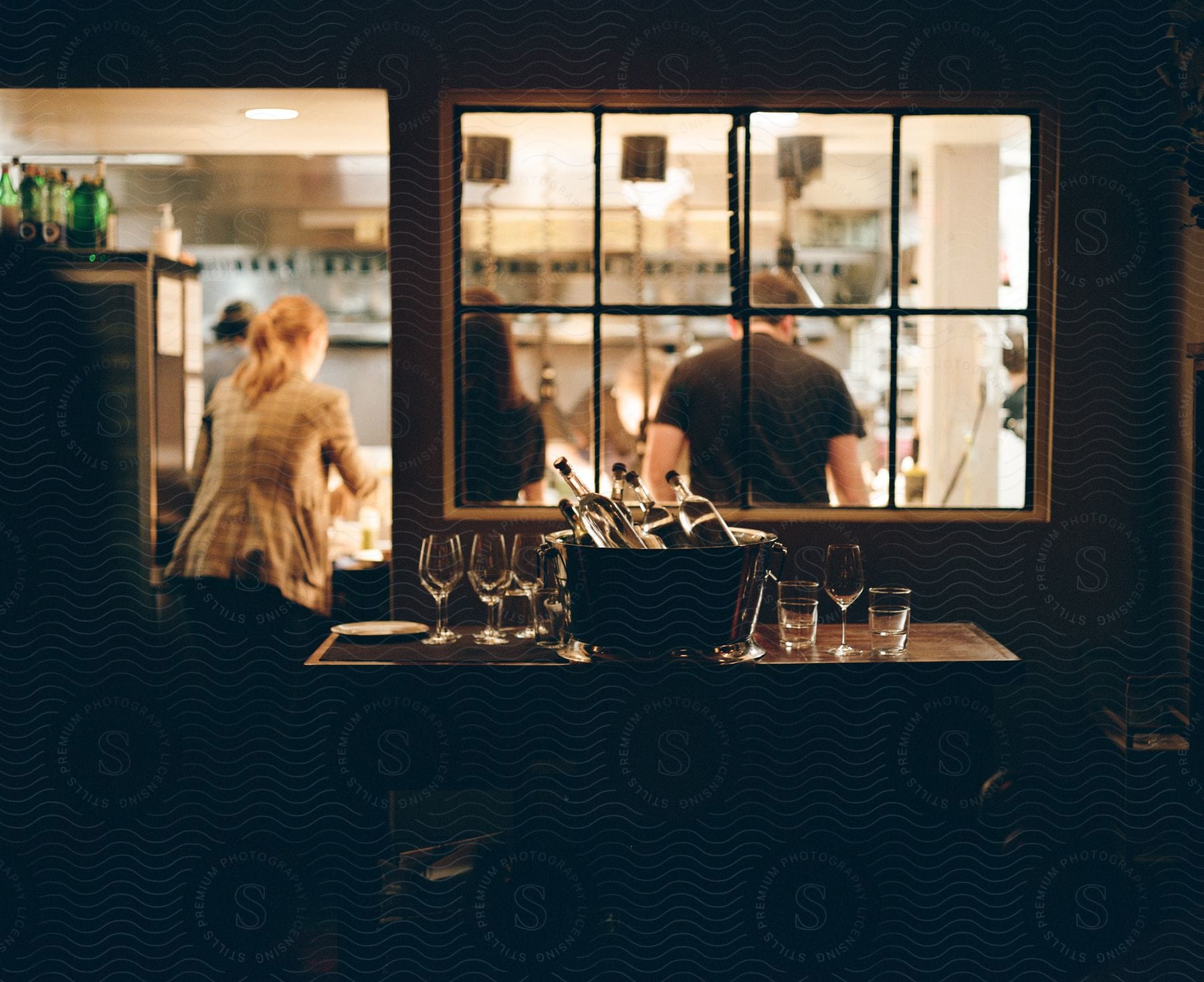 a table in a dark room is set up with glasses and wine as three people are seen outside the room from the window and door