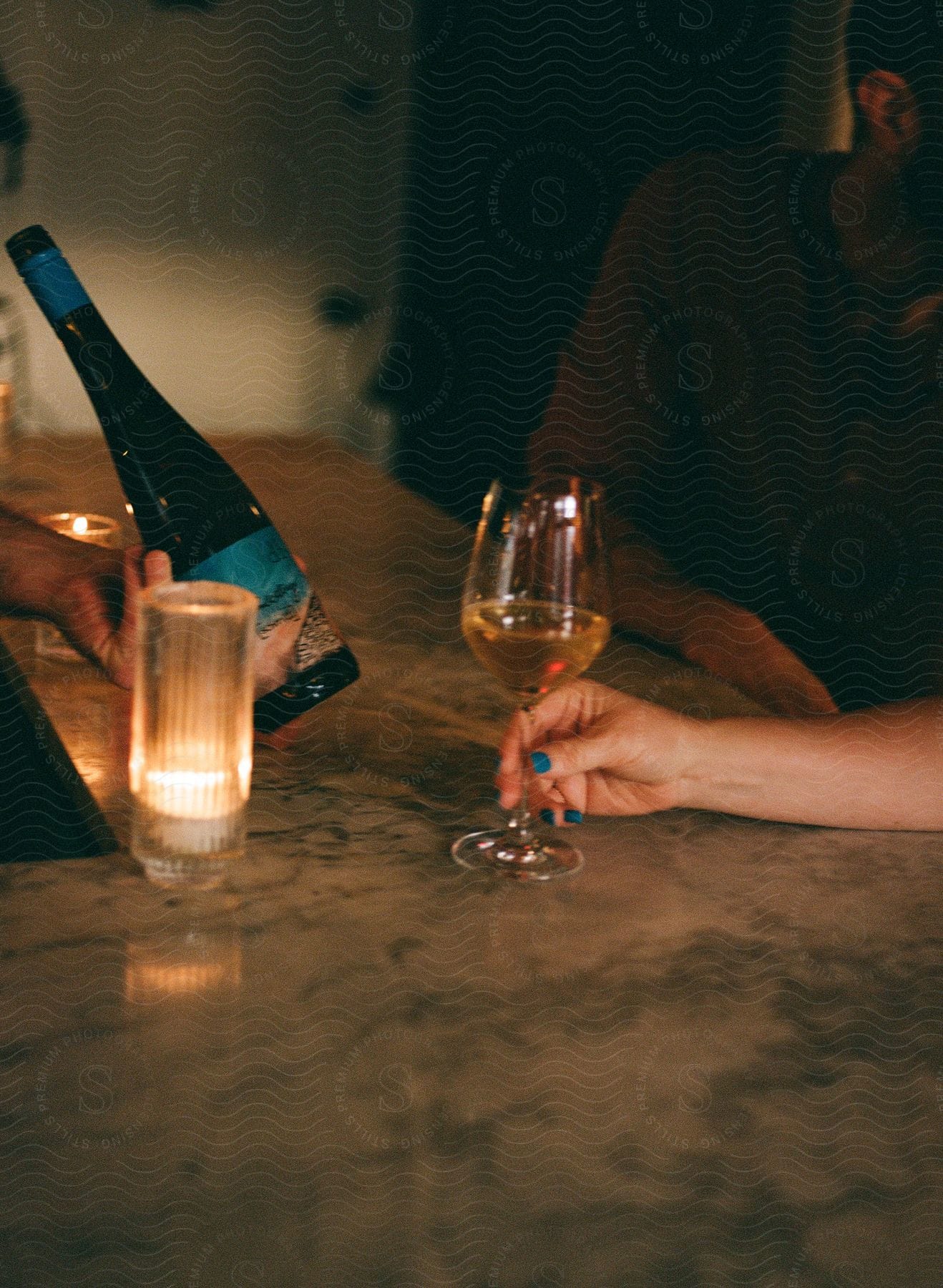 Close-up of a woman's hands holding a glass of white wine with the bottle in front of her.