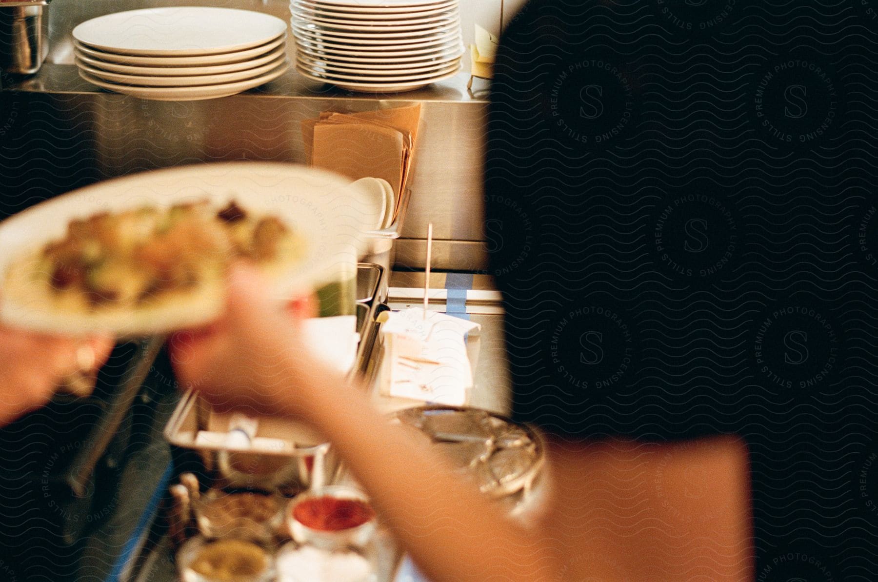 A cook stands in a kitchen holding a plate of food